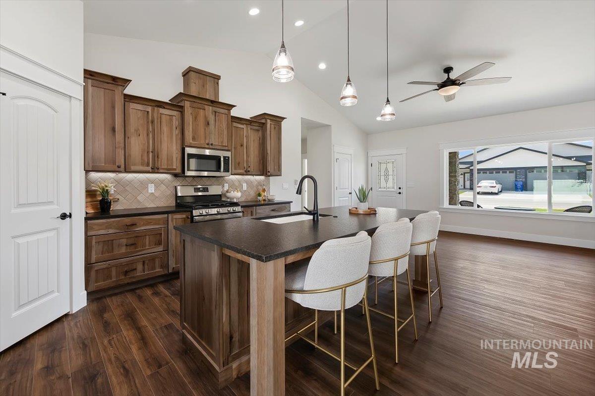 Kitchen with a center island with sink, decorative backsplash, hanging light fixtures, appliances with stainless steel finishes, and lofted ceiling