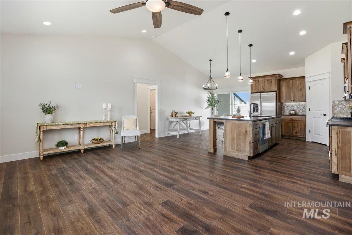 Kitchen with backsplash, decorative light fixtures, a kitchen island with sink, high vaulted ceiling, and a kitchen breakfast bar