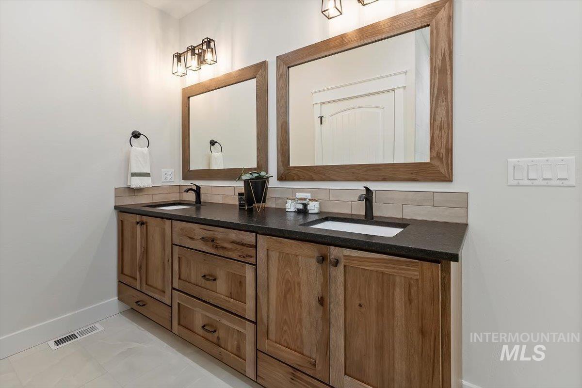 Full bath with double vanity, tasteful backsplash, and light tile patterned floors