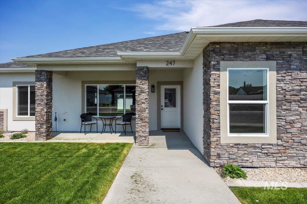 Doorway to property featuring stone siding, stucco siding, and a shingled roof