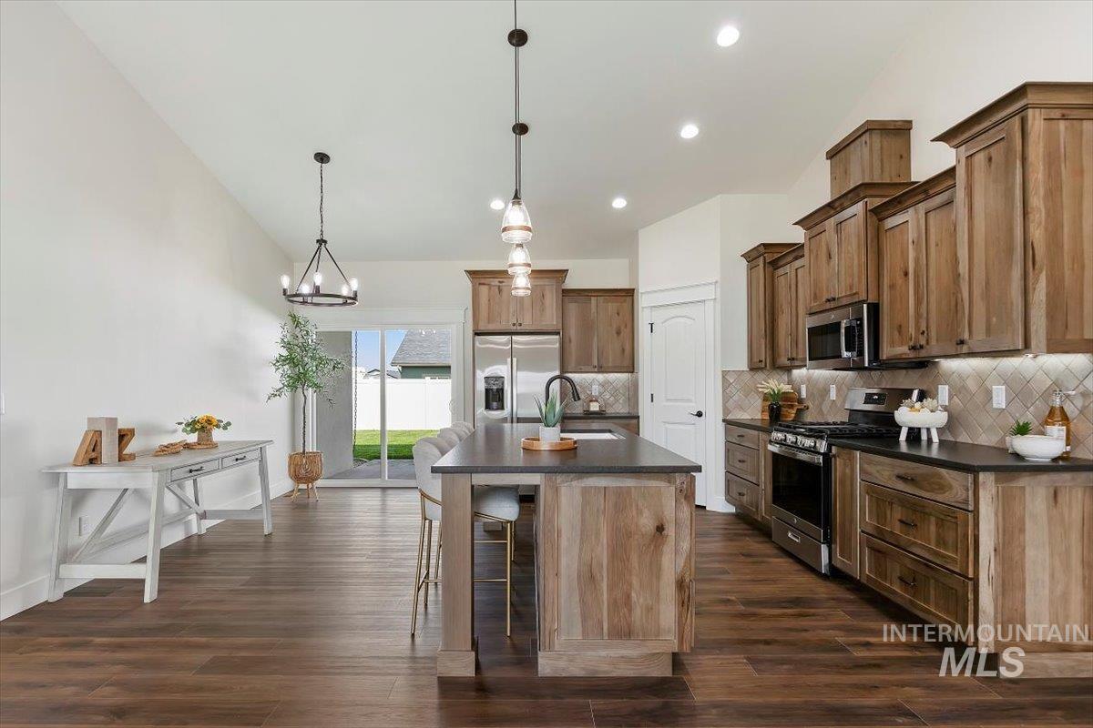 Kitchen featuring dark countertops, appliances with stainless steel finishes, decorative backsplash, an island with sink, and a breakfast bar area