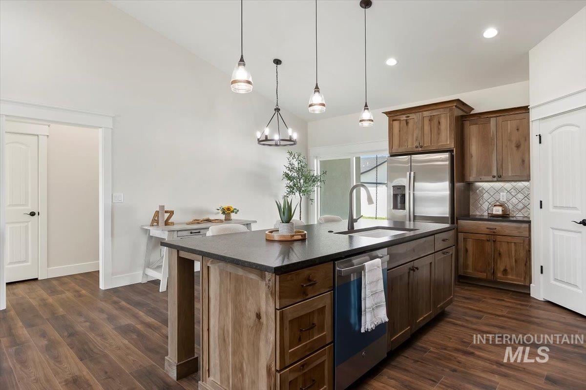 Kitchen with tasteful backsplash, stainless steel appliances, decorative light fixtures, a center island with sink, and dark wood finished floors