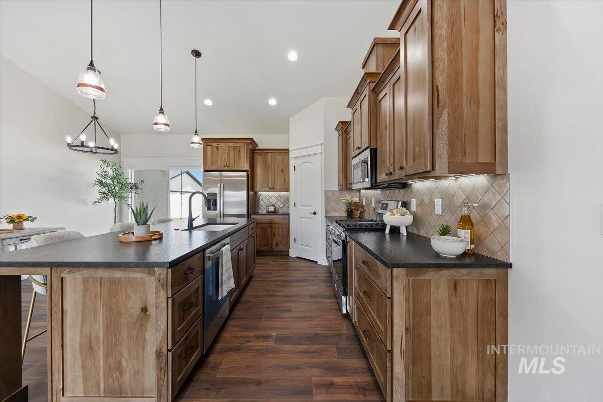 Kitchen with dark countertops, a kitchen bar, stainless steel appliances, hanging light fixtures, and dark wood-style flooring