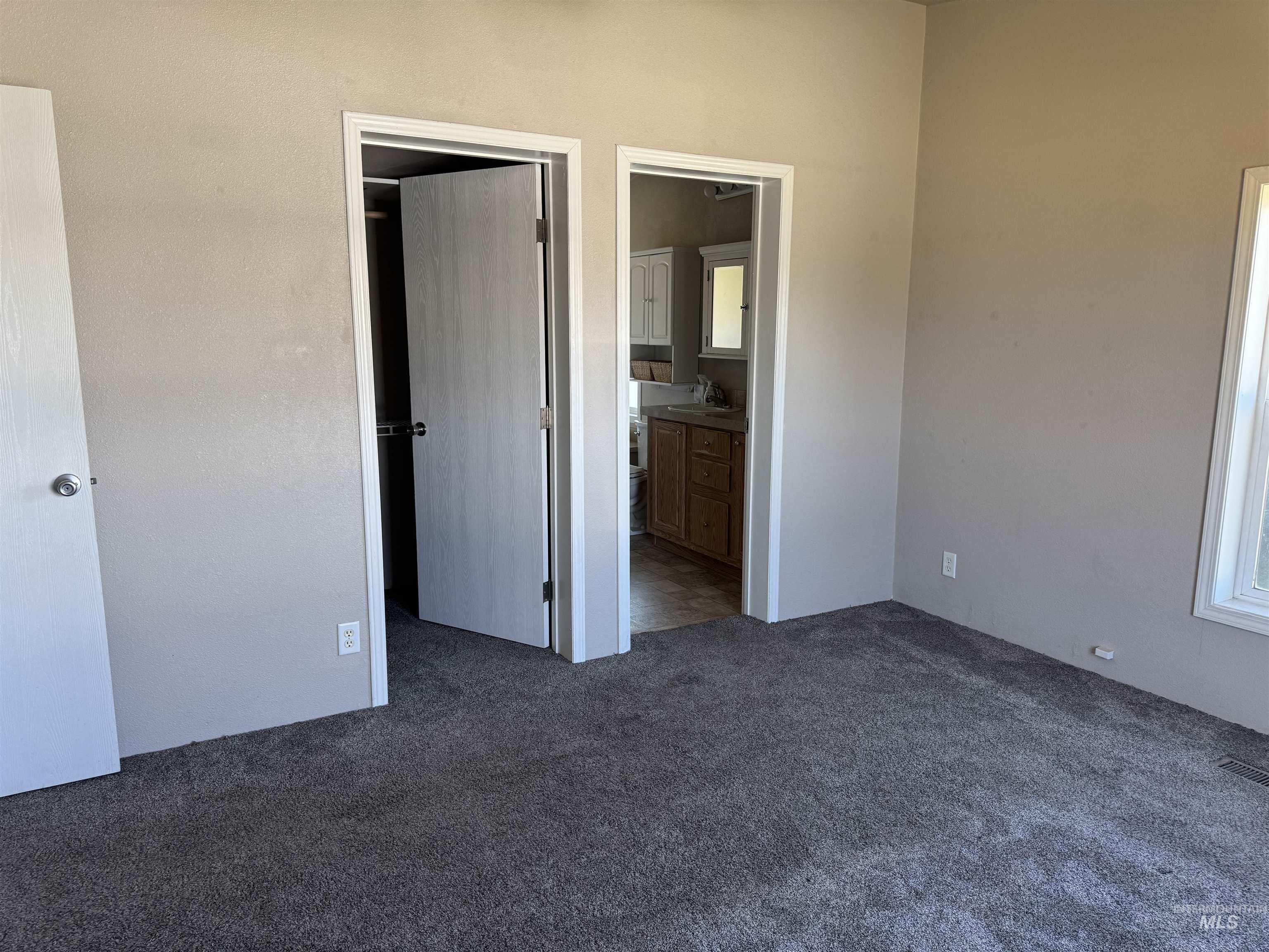 Unfurnished bedroom featuring dark carpet and connected bathroom