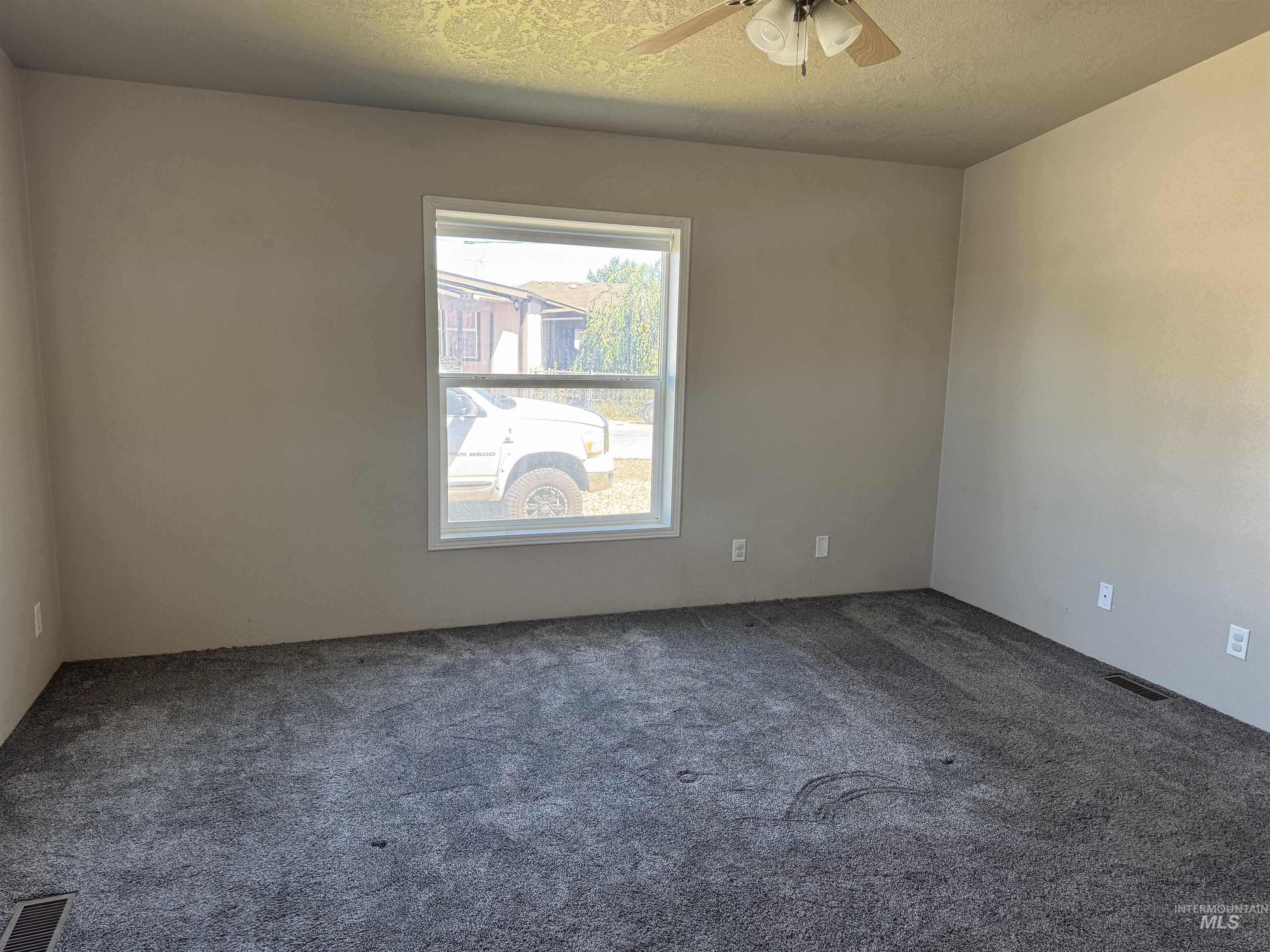 Carpeted empty room featuring ceiling fan and a textured ceiling