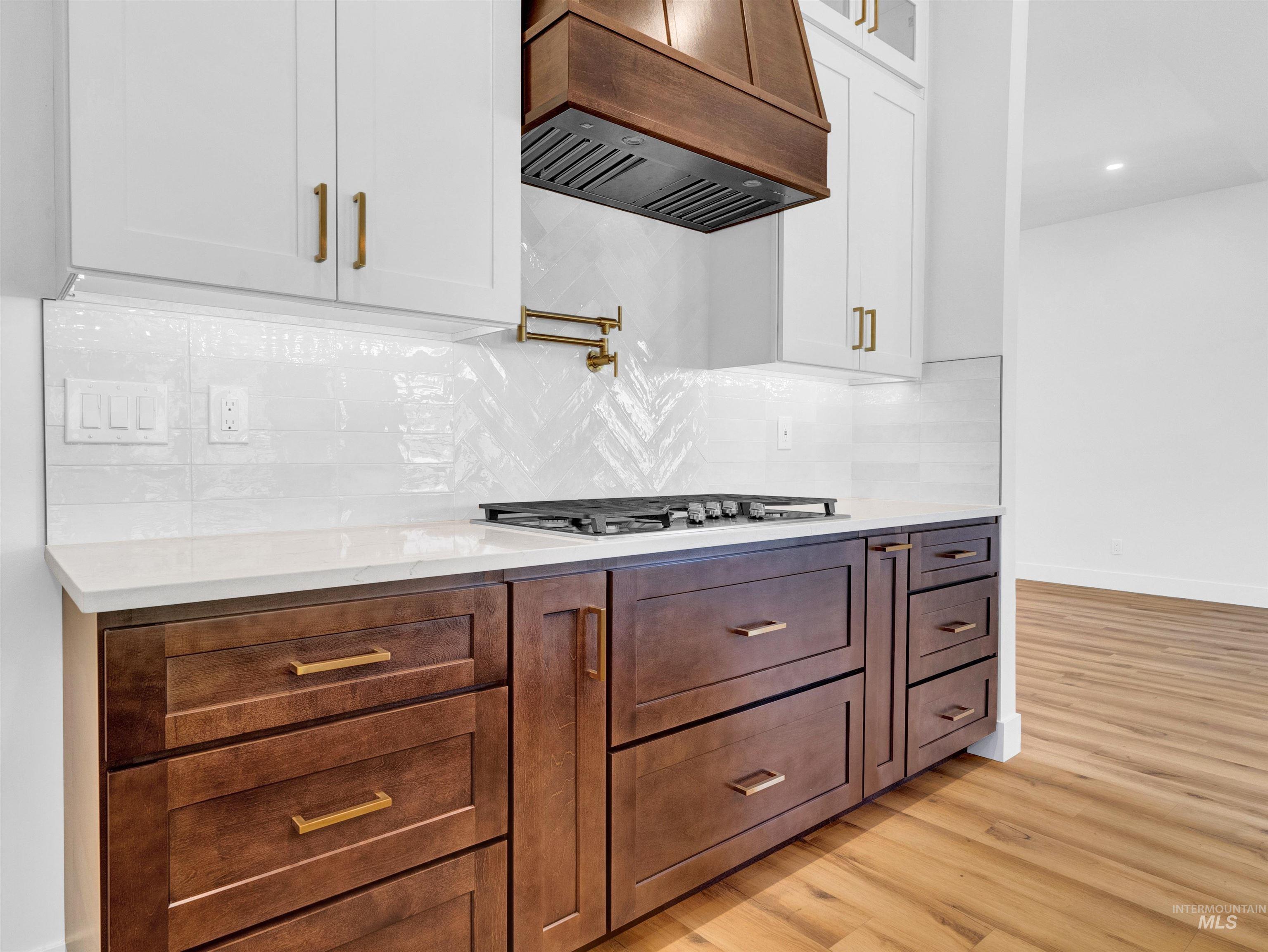 Kitchen featuring light wood-type flooring, premium range hood, white cabinetry, decorative backsplash, and glass insert cabinets