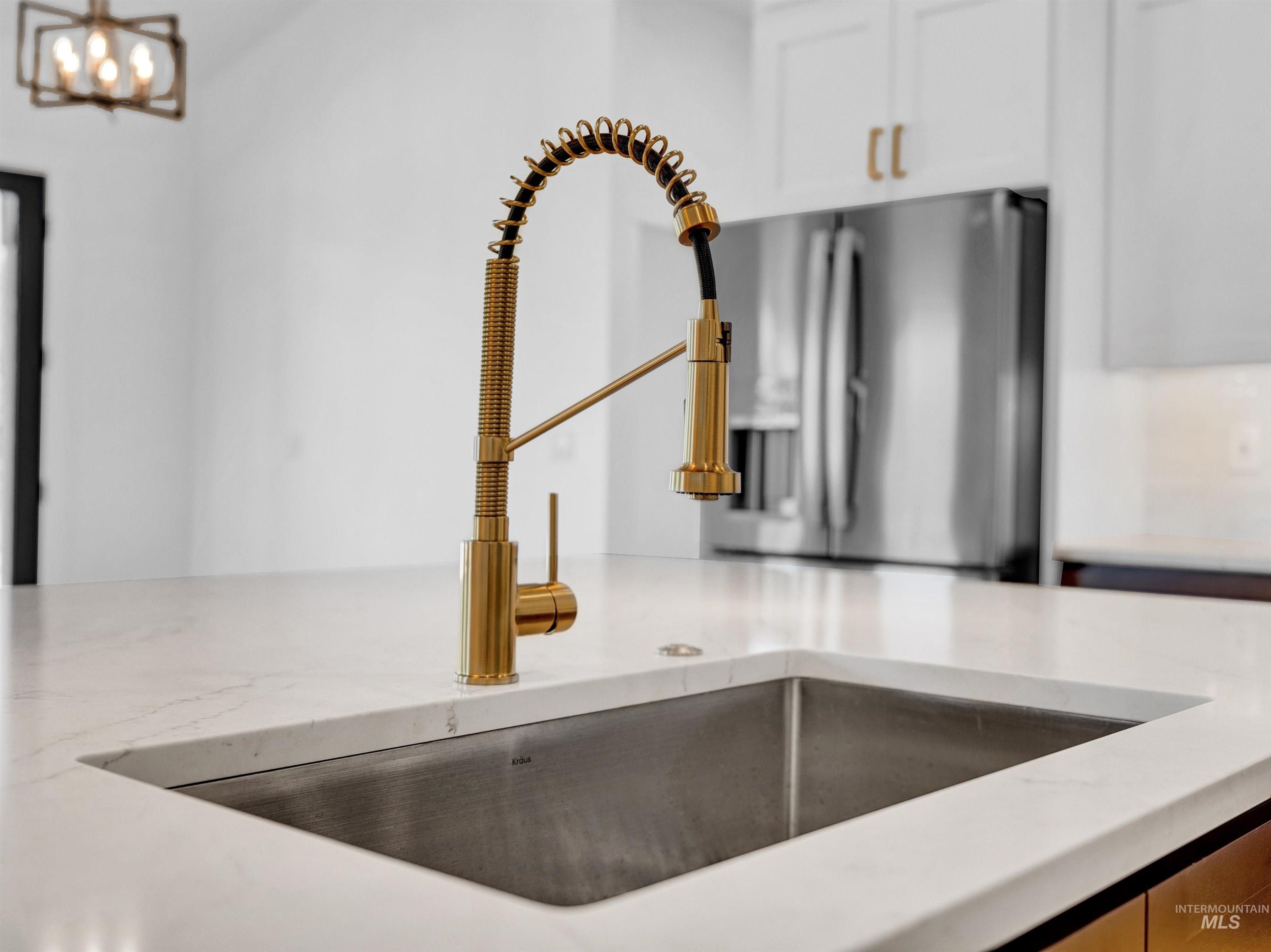 Kitchen view of white cabinets, a chandelier, and light stone countertops