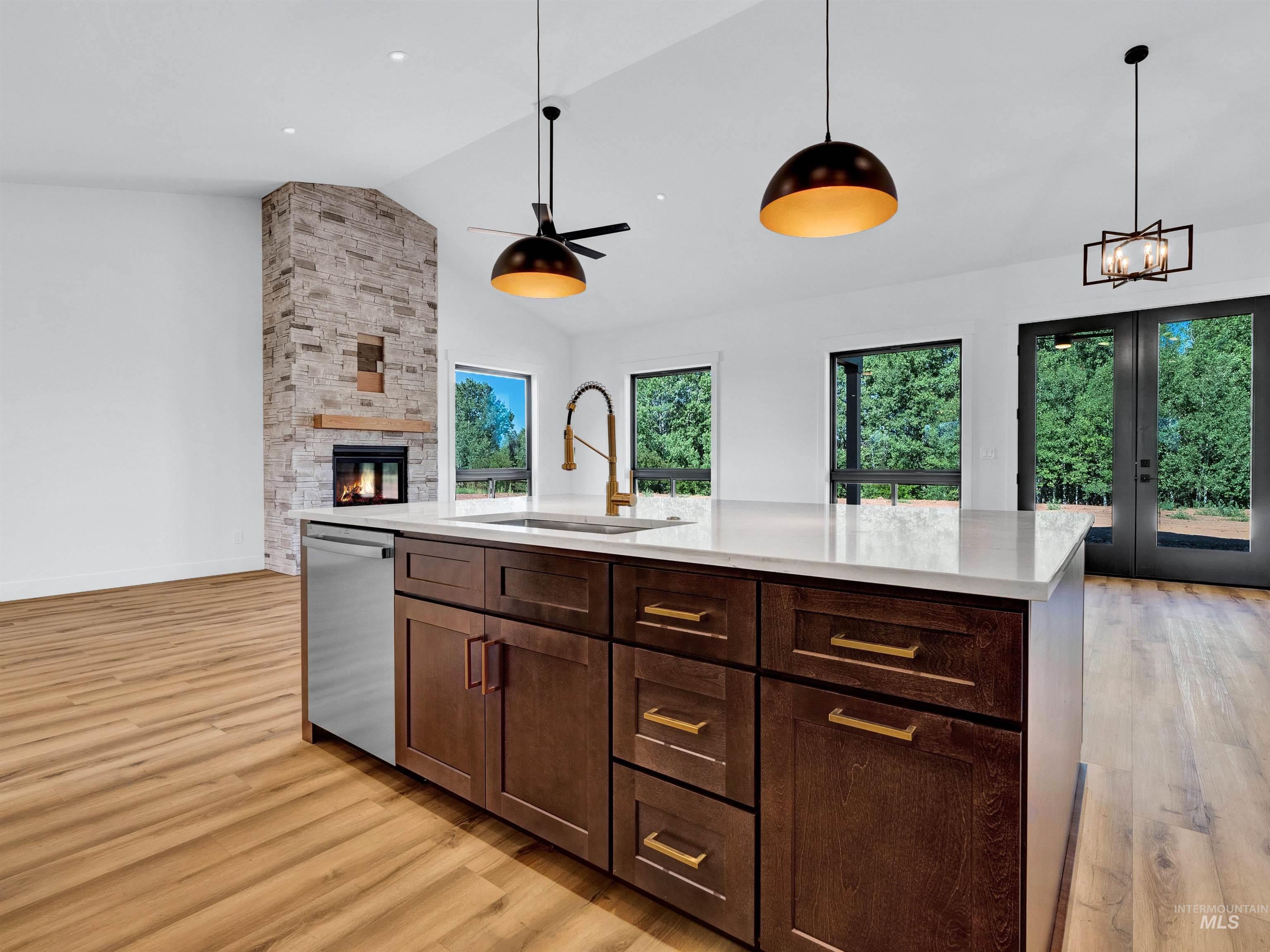 Kitchen featuring light wood-style floors, open floor plan, a stone fireplace, decorative light fixtures, and high vaulted ceiling