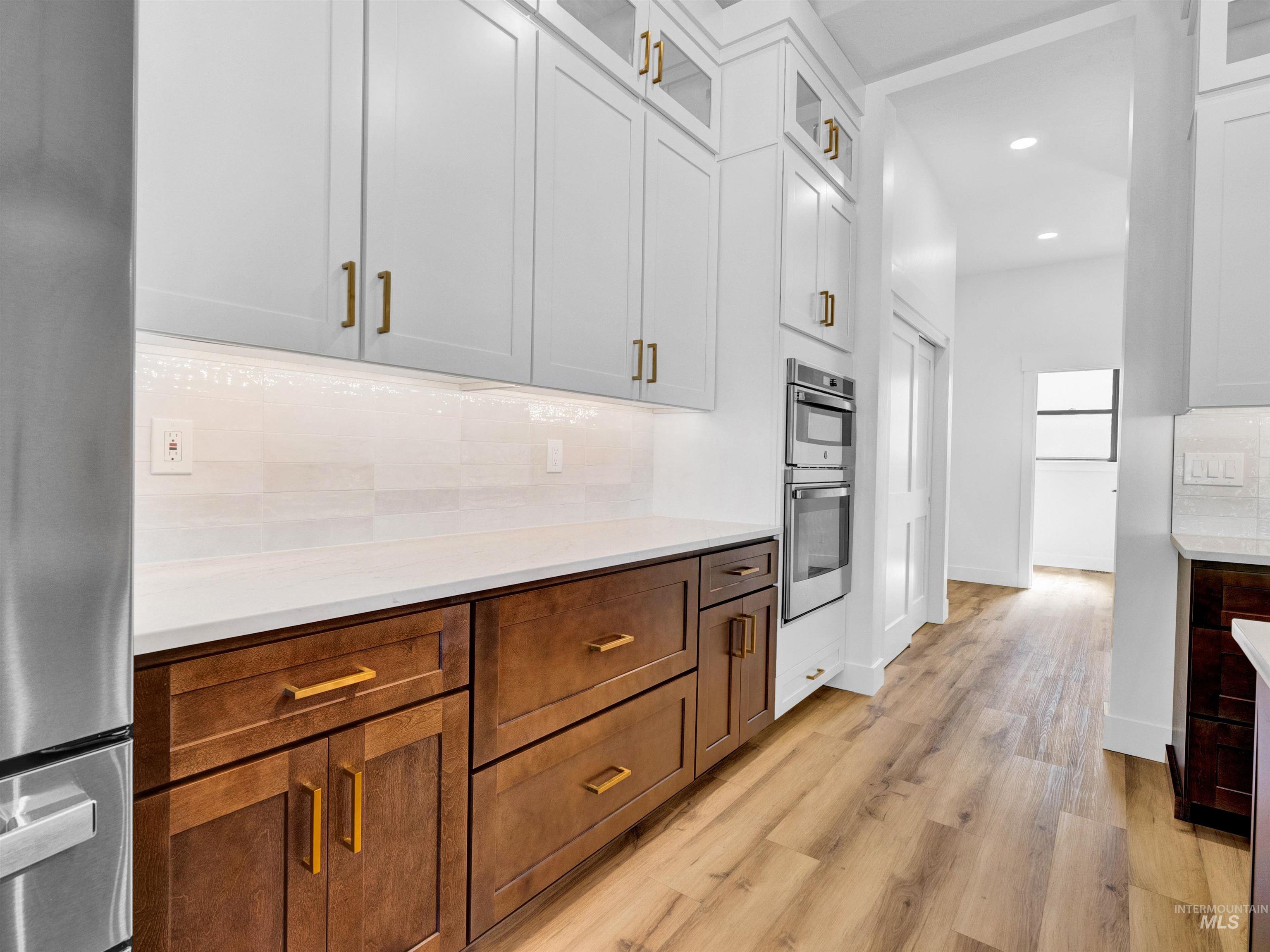 Kitchen with tasteful backsplash, appliances with stainless steel finishes, light countertops, light wood-type flooring, and recessed lighting
