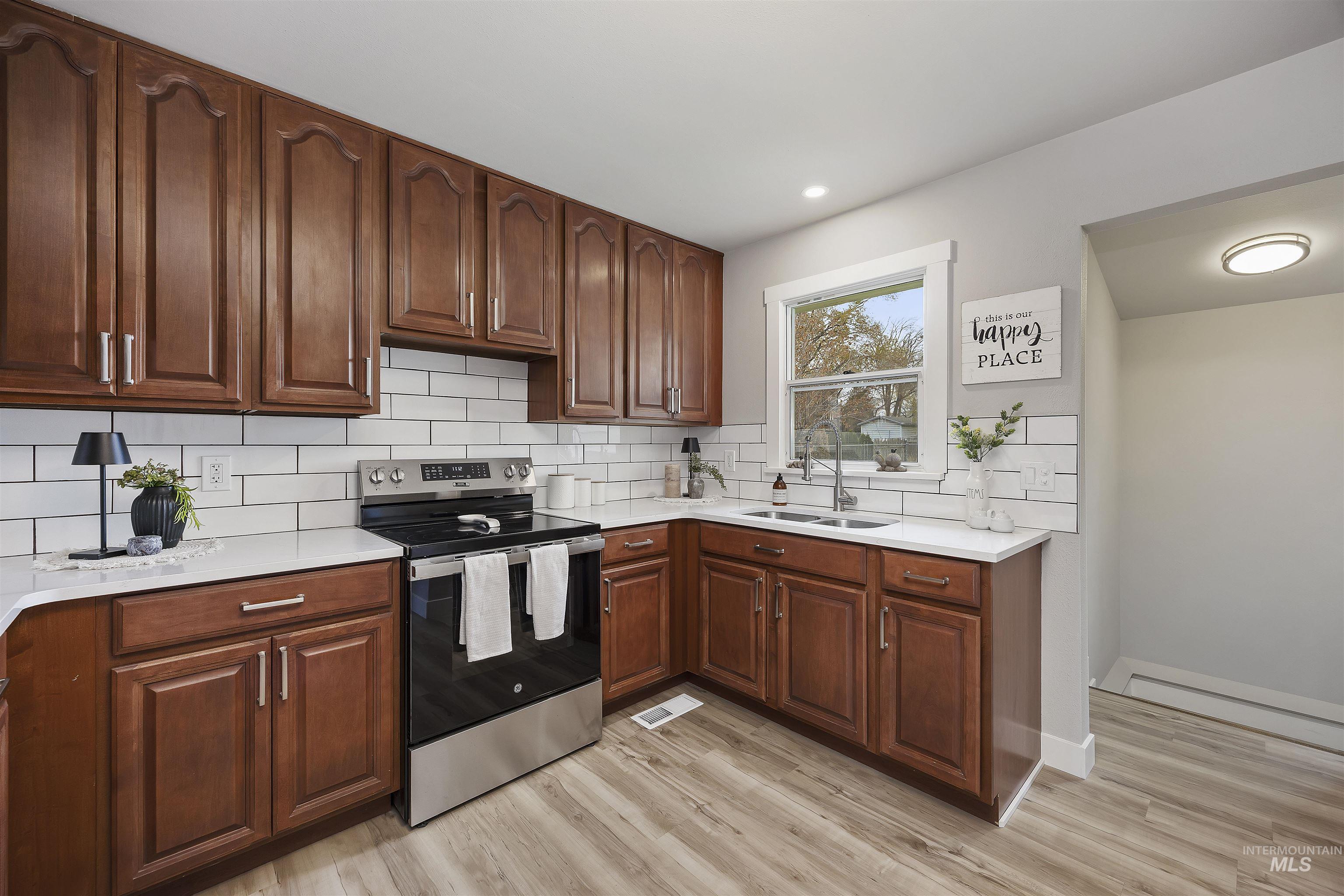 Kitchen featuring stainless steel electric stove, decorative backsplash, light wood-style flooring, and recessed lighting