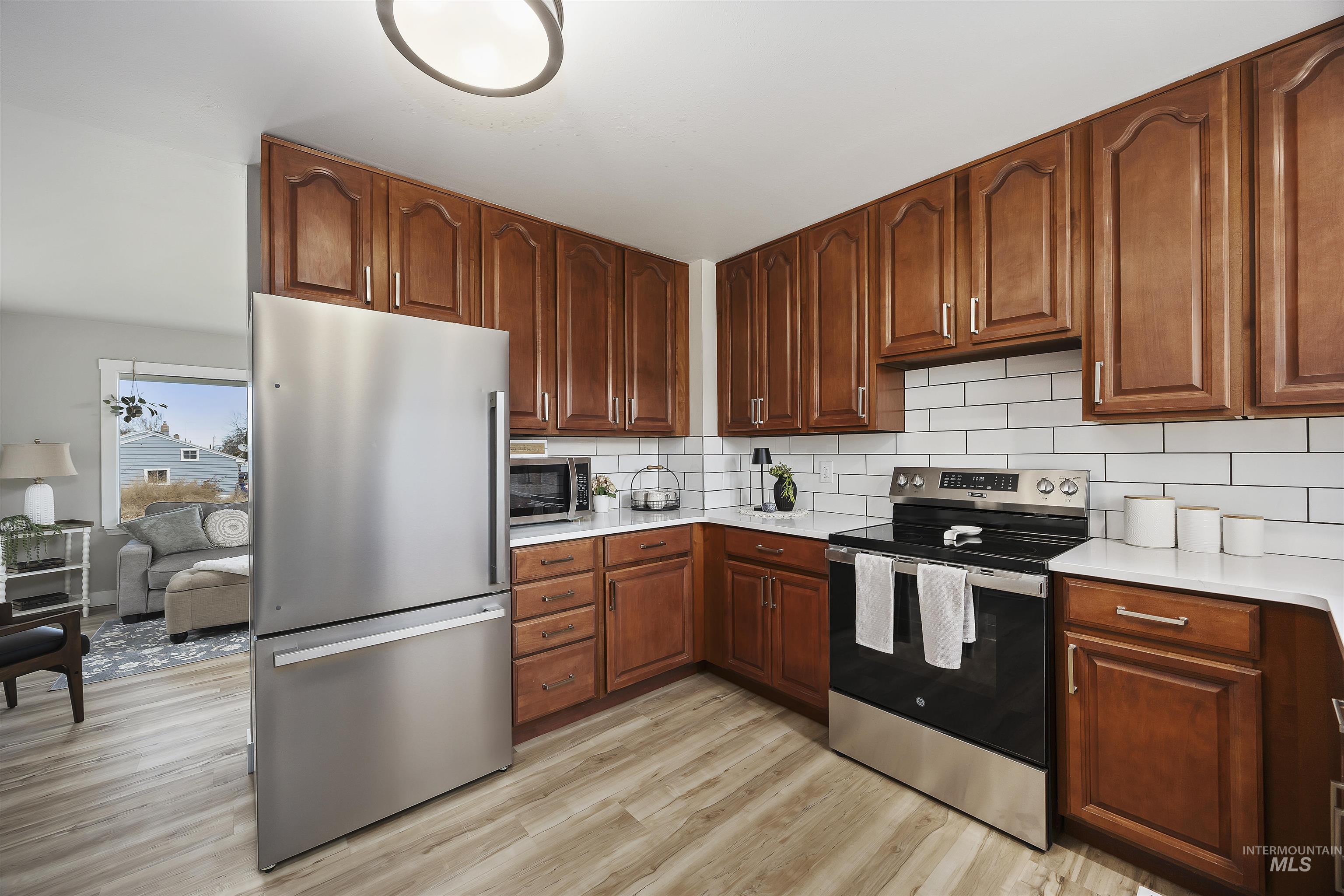 Kitchen with stainless steel appliances, decorative backsplash, light wood finished floors, and light stone counters