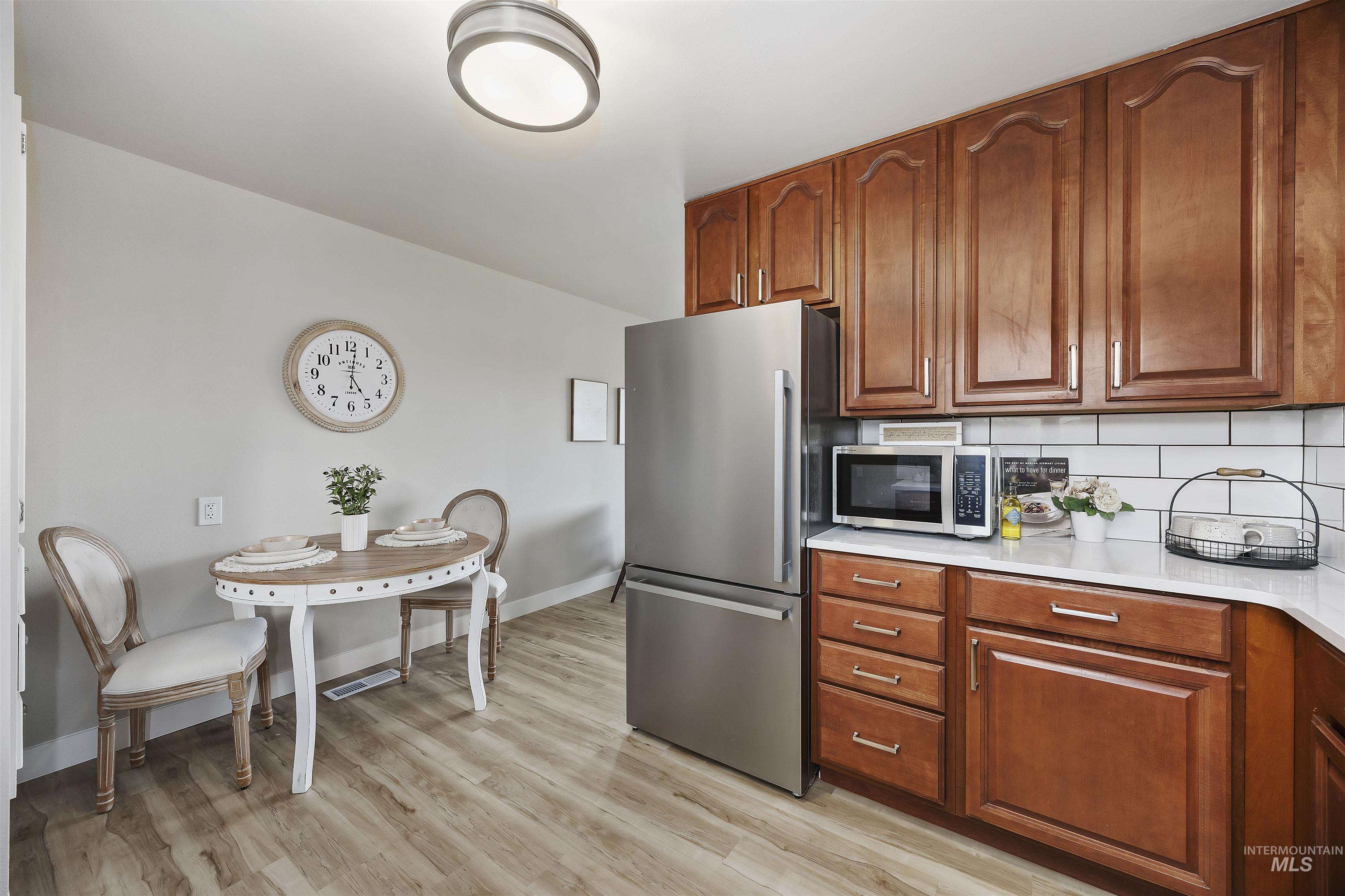 Kitchen featuring stainless steel appliances, backsplash, light wood-style floors, brown cabinets, and light stone counters