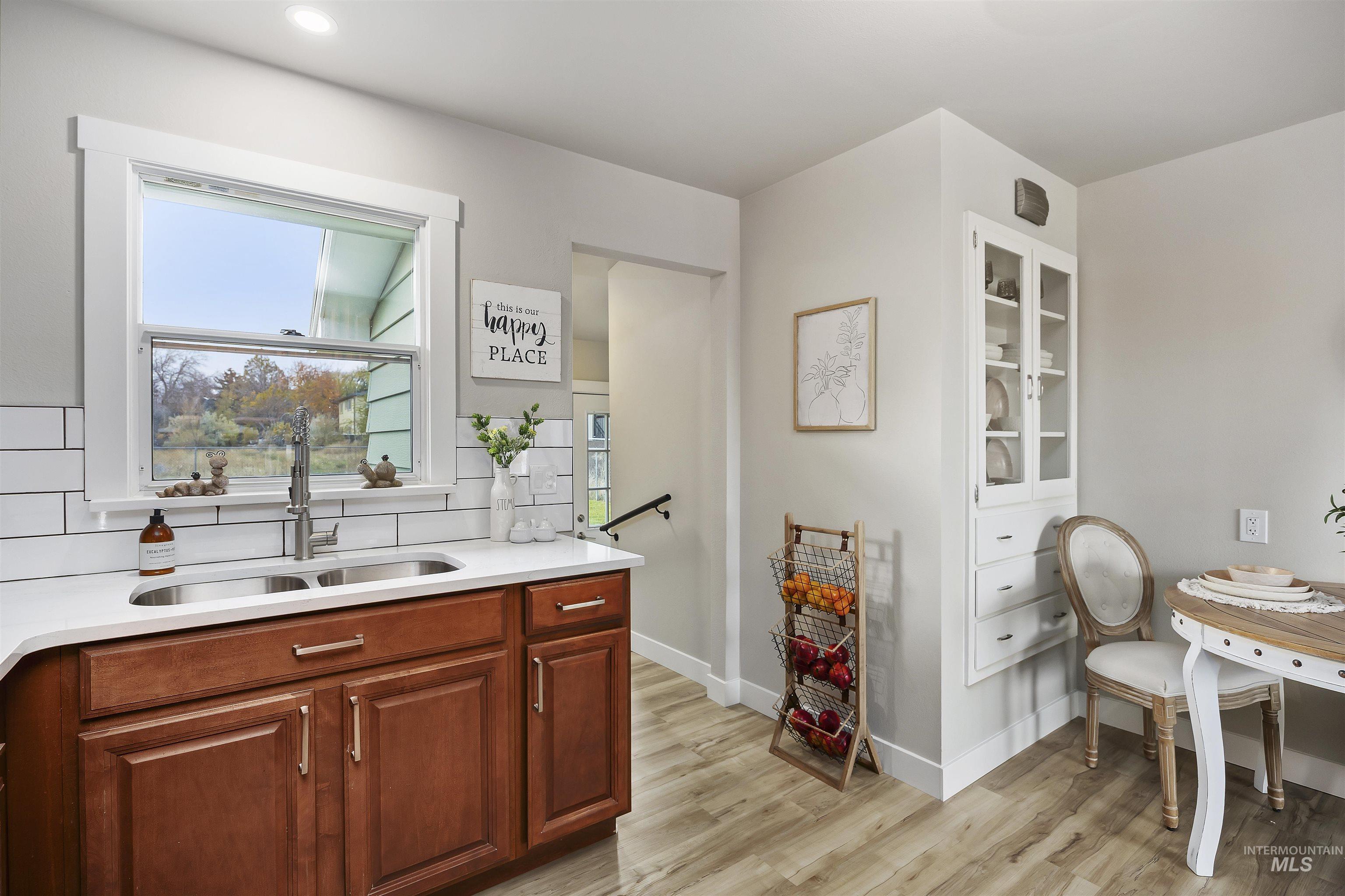 Kitchen featuring light wood-style flooring, glass insert cabinets, light stone counters, and brown cabinets