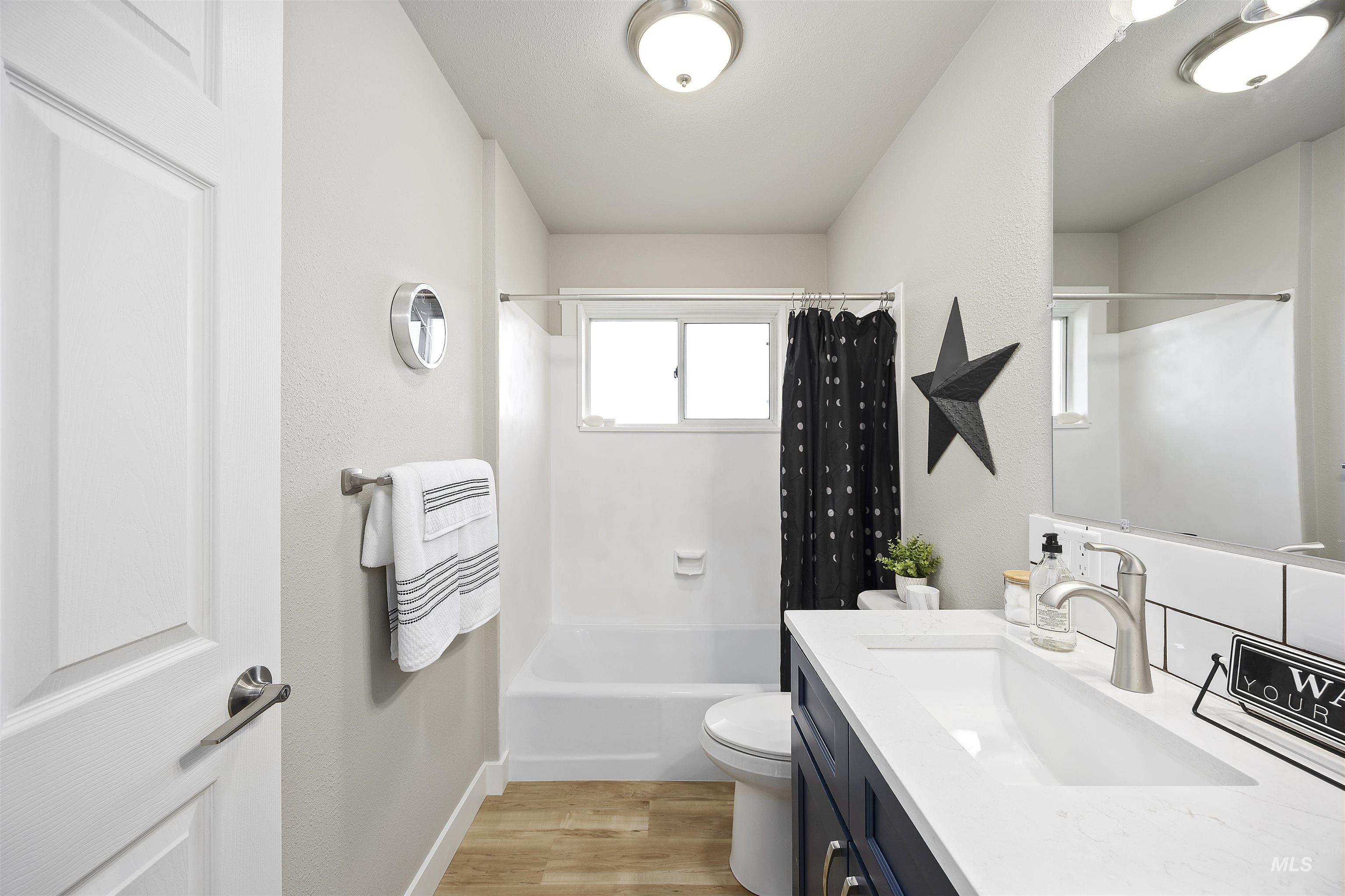 Full bath with light wood finished floors, shower / tub combo with curtain, vanity, and a textured wall