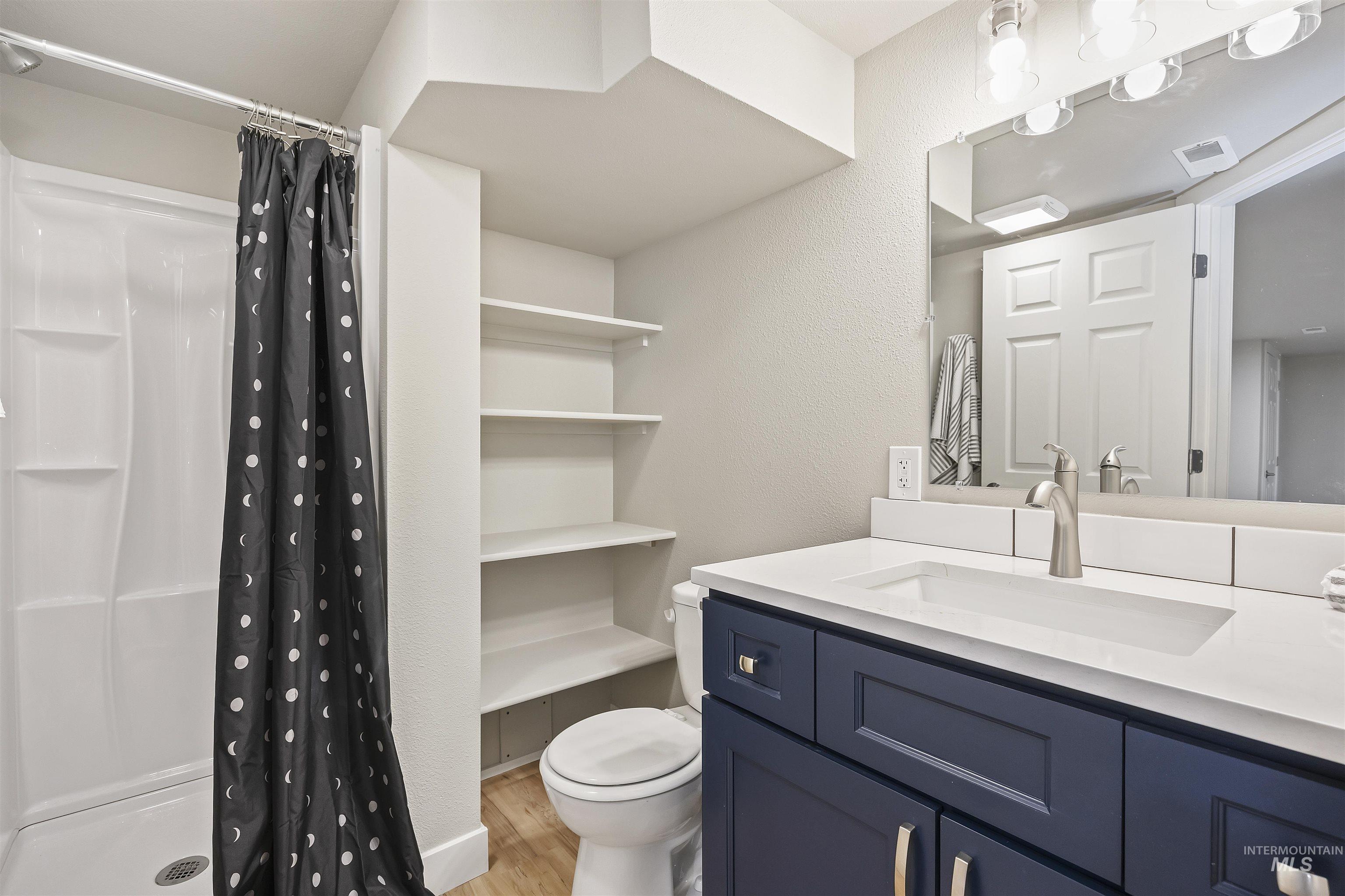 Bathroom featuring a shower stall, light wood finished floors, vanity, and a textured wall