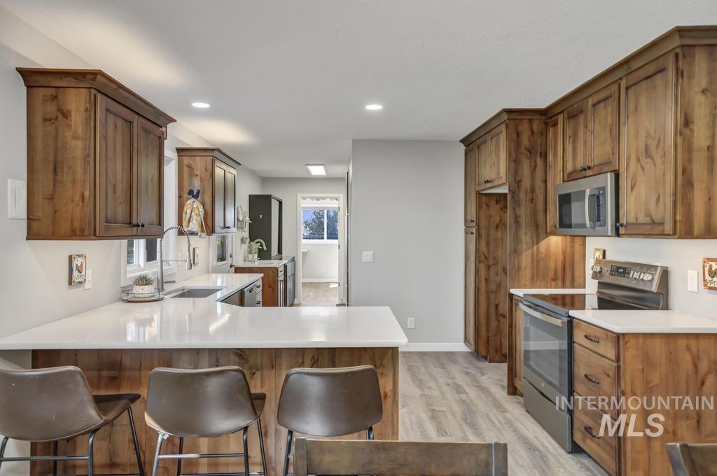 Kitchen featuring brown cabinetry, appliances with stainless steel finishes, a peninsula, light wood-type flooring, and a kitchen breakfast bar