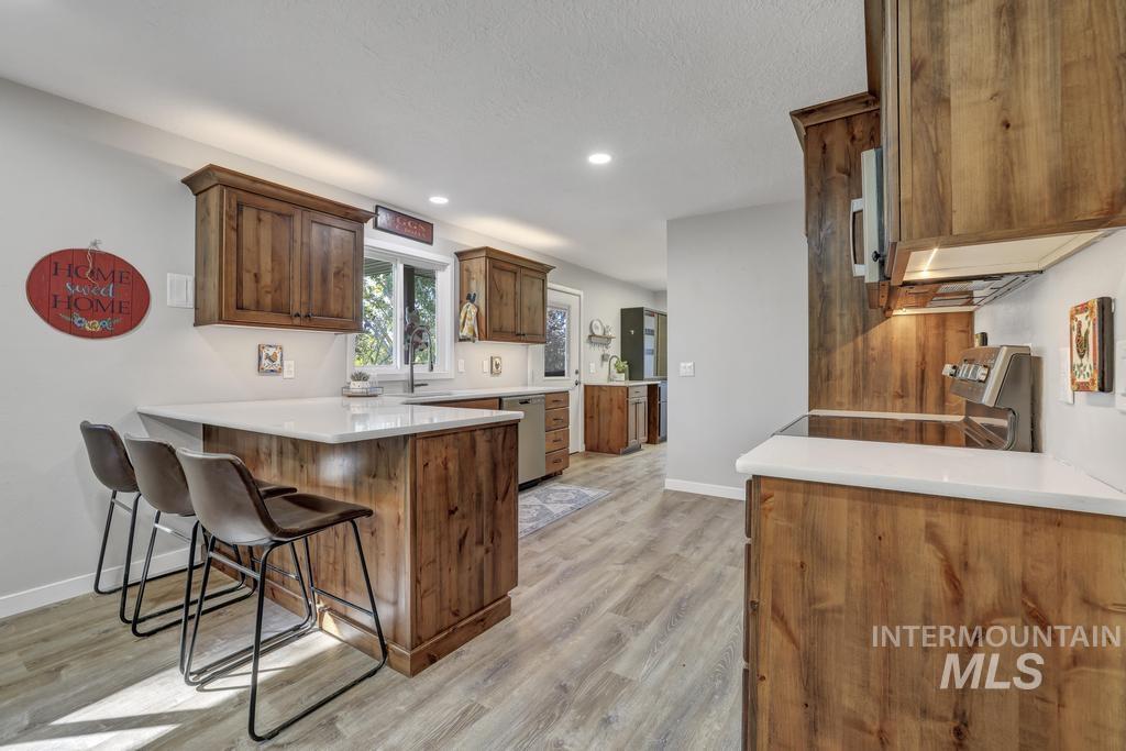 Kitchen with a peninsula, a kitchen breakfast bar, stainless steel appliances, light wood finished floors, and recessed lighting