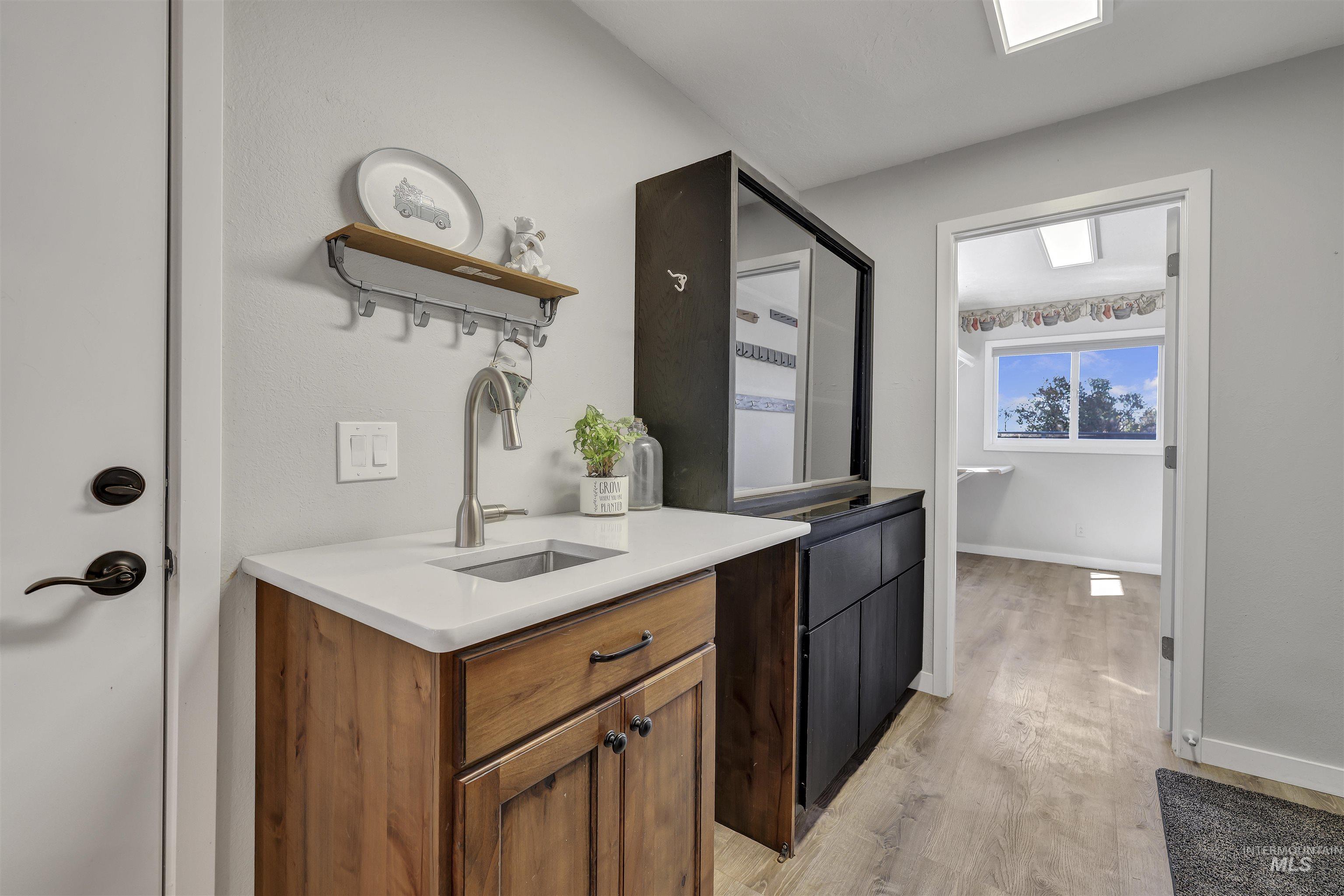 Bar area featuring open shelves, light wood finished floors, brown cabinetry, and light stone counters