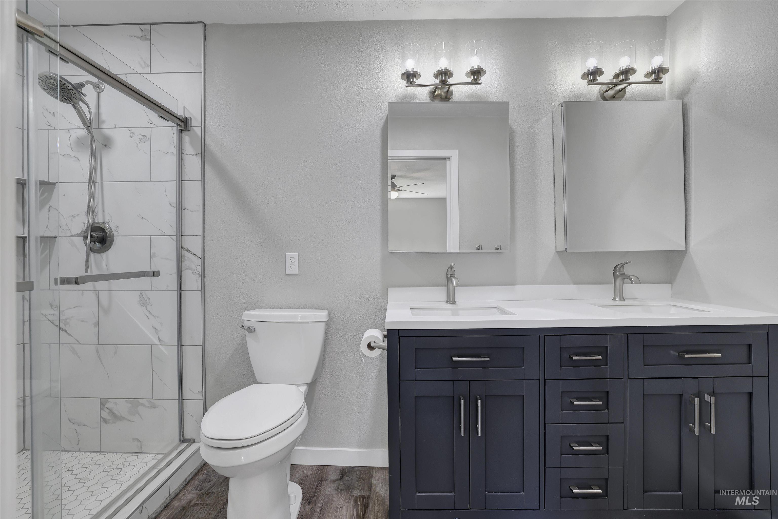 Full bathroom with a marble finish shower, double vanity, and dark wood-style flooring
