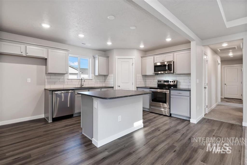 Kitchen with stainless steel appliances, dark countertops, dark wood finished floors, a kitchen island, and recessed lighting