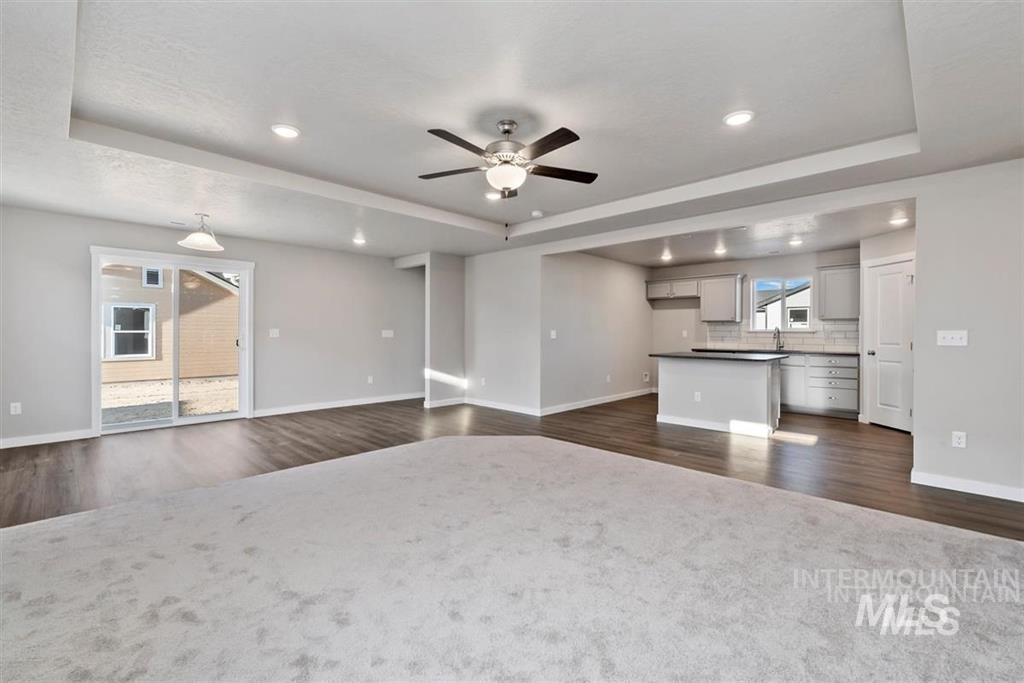 Unfurnished living room with a tray ceiling, dark wood-style floors, a ceiling fan, and recessed lighting