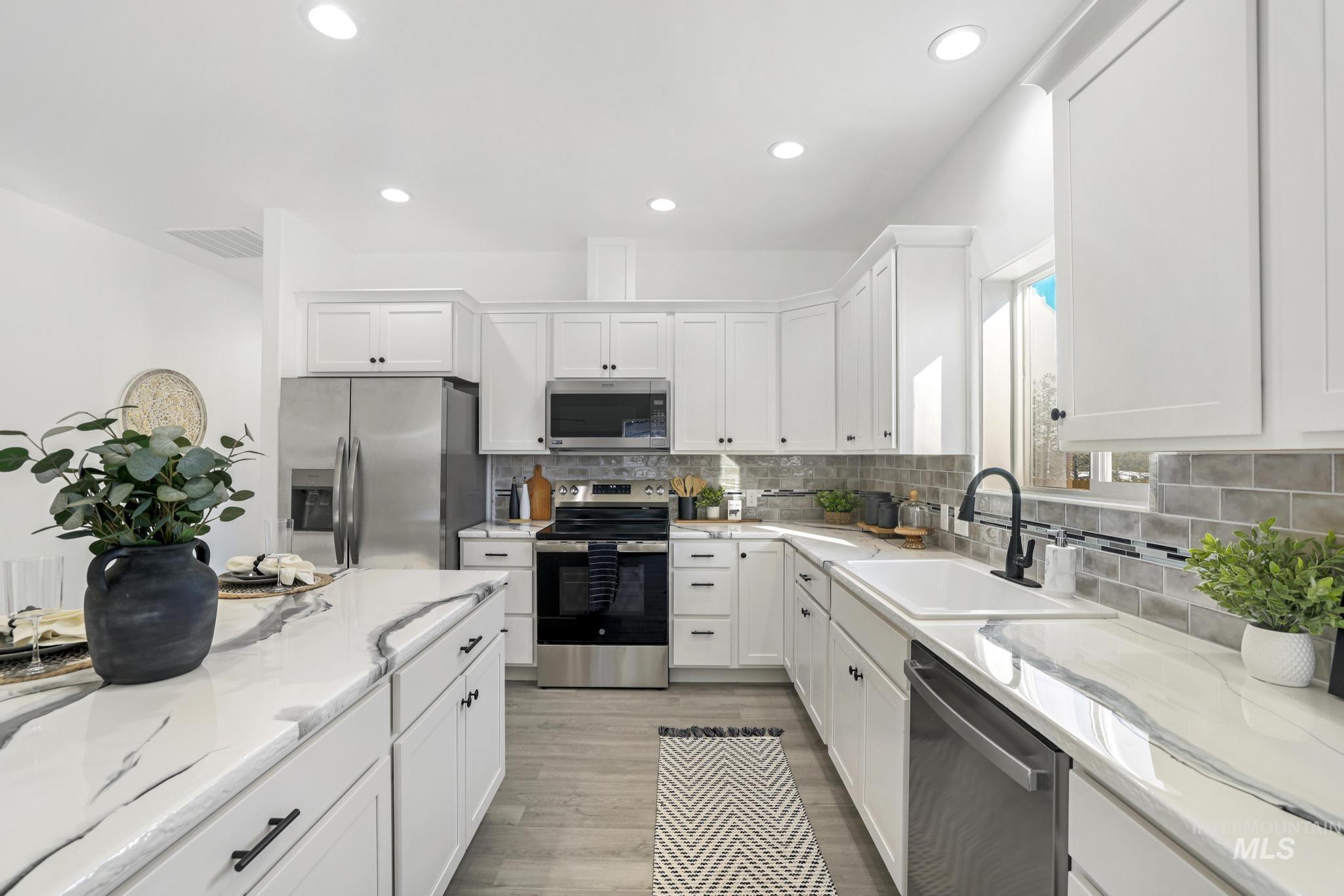 Kitchen with appliances with stainless steel finishes, backsplash, white cabinets, light stone counters, and recessed lighting