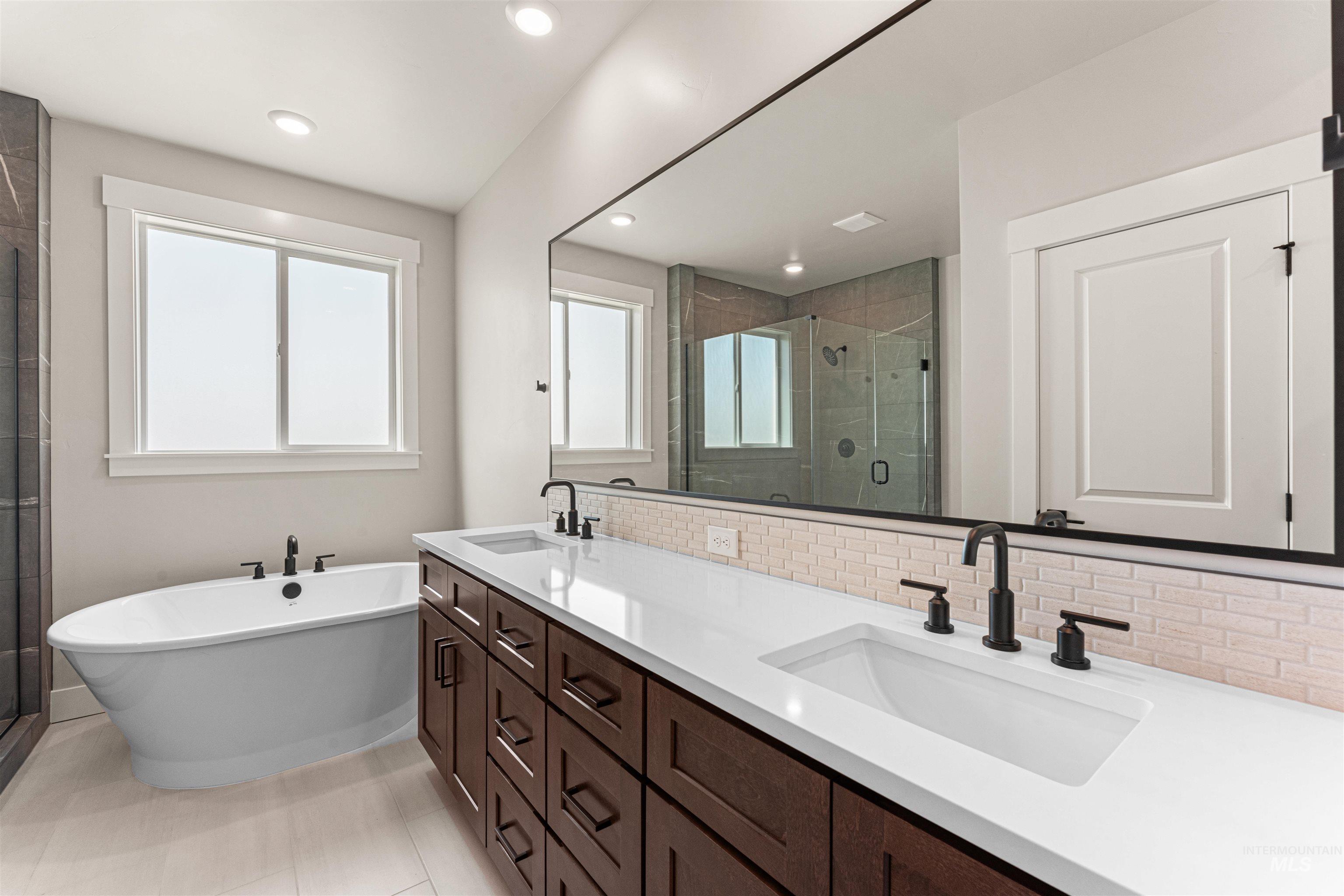 Full bath with a stall shower, tasteful backsplash, double vanity, a soaking tub, and recessed lighting