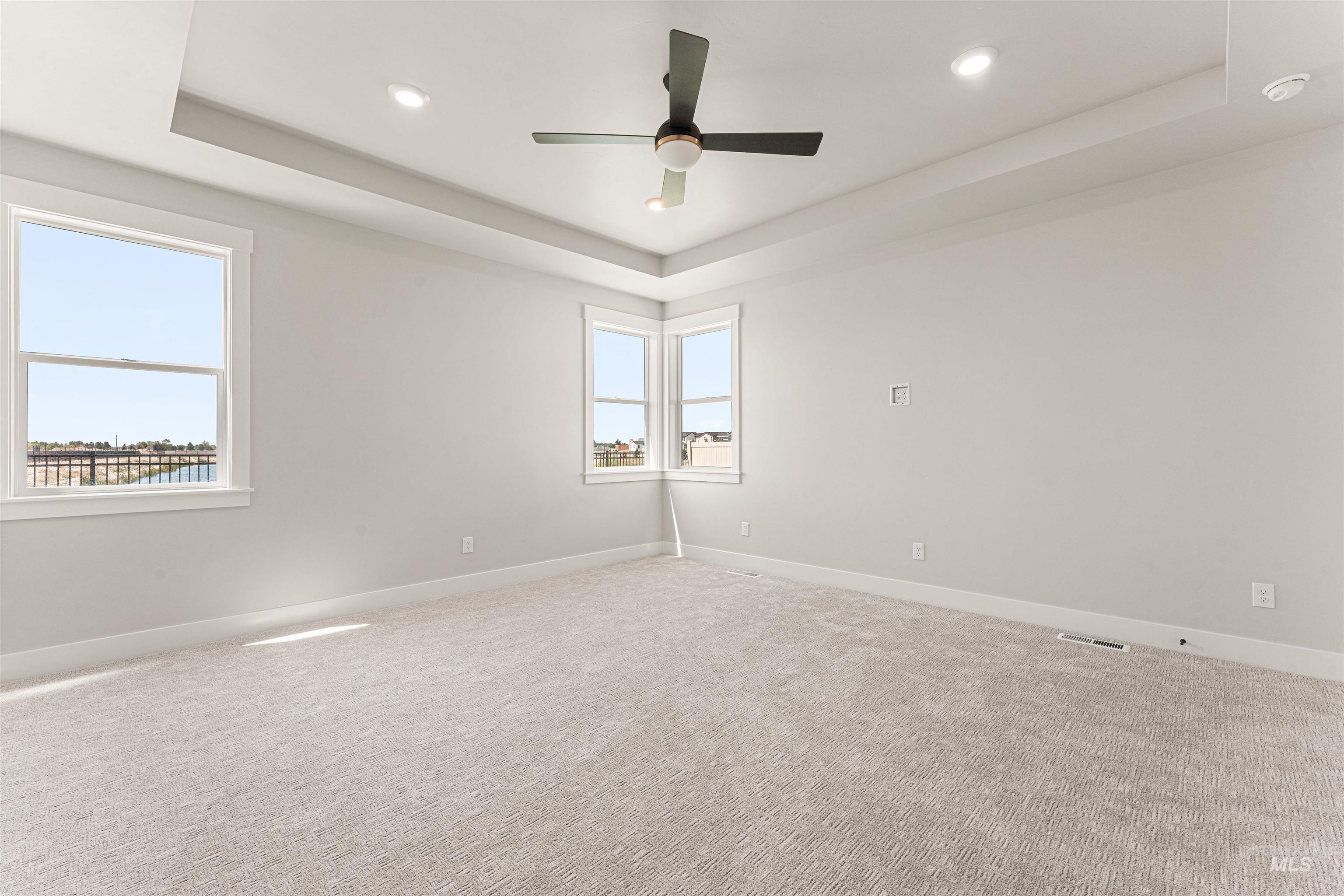 Empty room with a tray ceiling, carpet floors, recessed lighting, and a ceiling fan