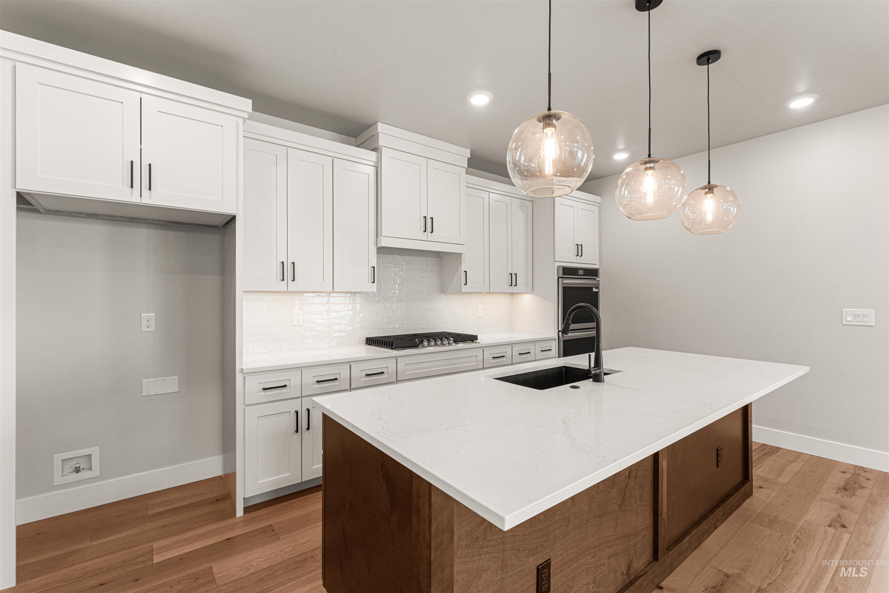 Kitchen with a kitchen island with sink, white cabinets, decorative light fixtures, recessed lighting, and light wood-type flooring