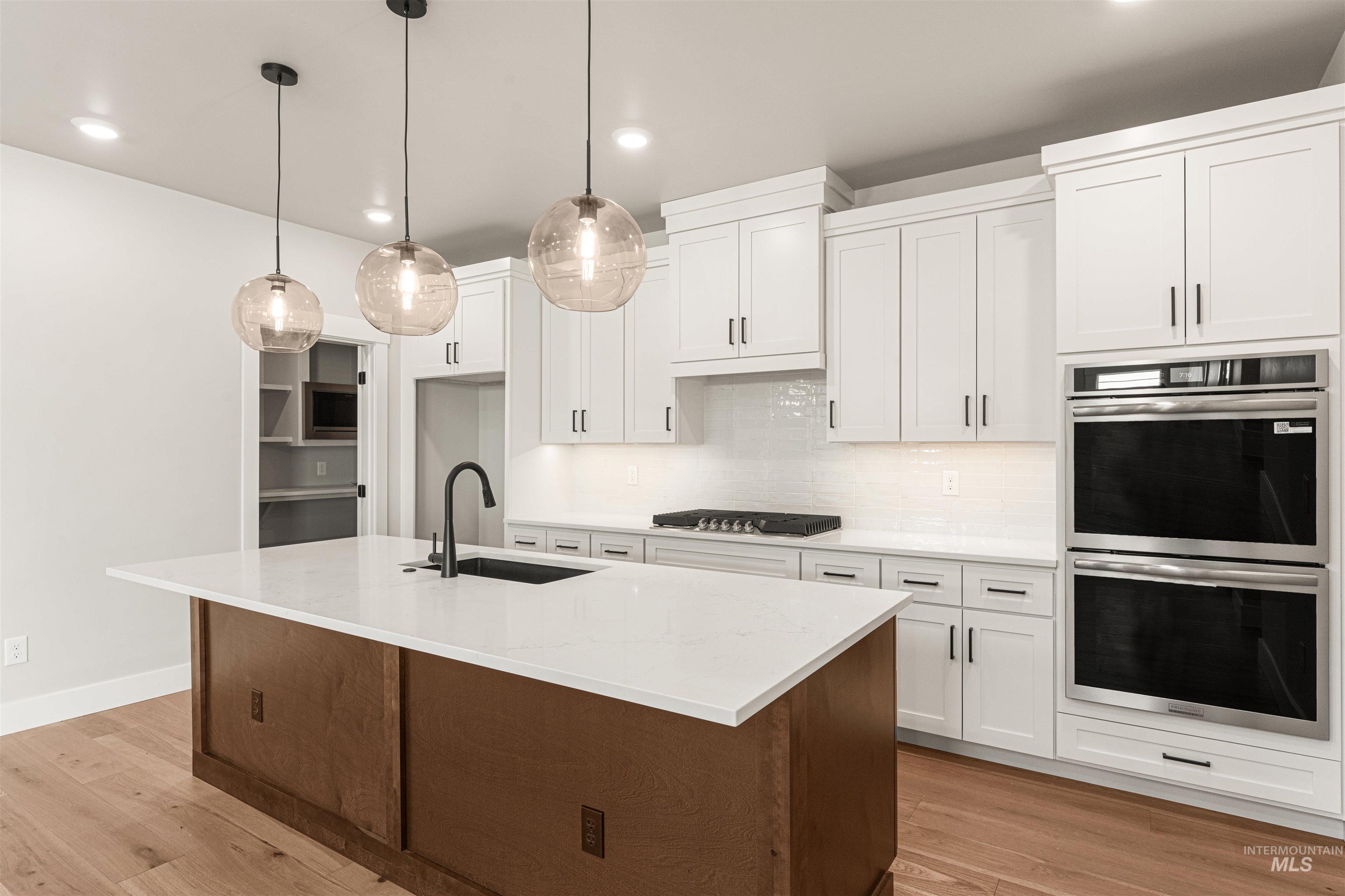 Kitchen featuring stainless steel appliances, recessed lighting, light wood-type flooring, white cabinets, and a center island with sink