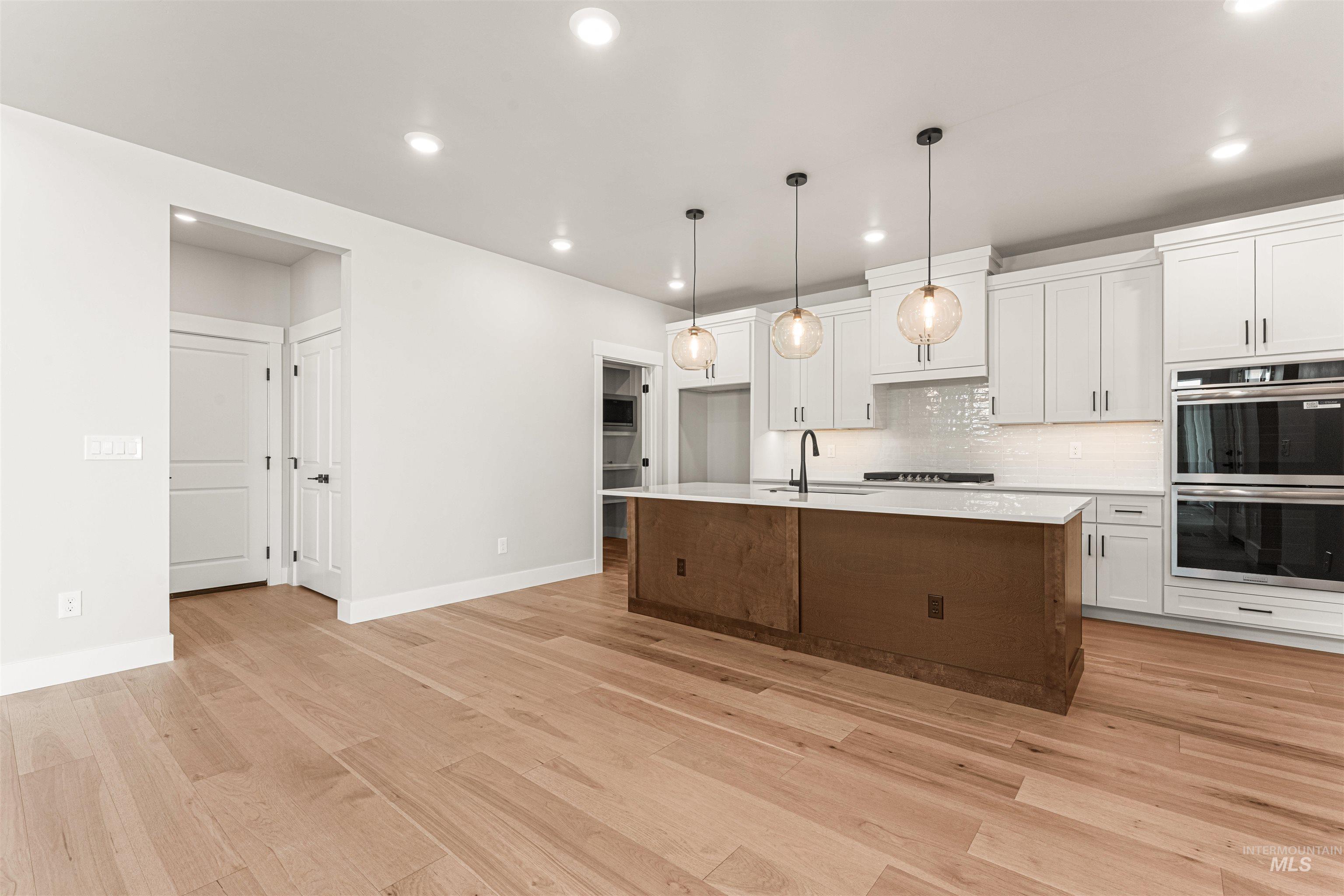 Kitchen with stainless steel double oven, recessed lighting, light wood-style flooring, light countertops, and white cabinetry