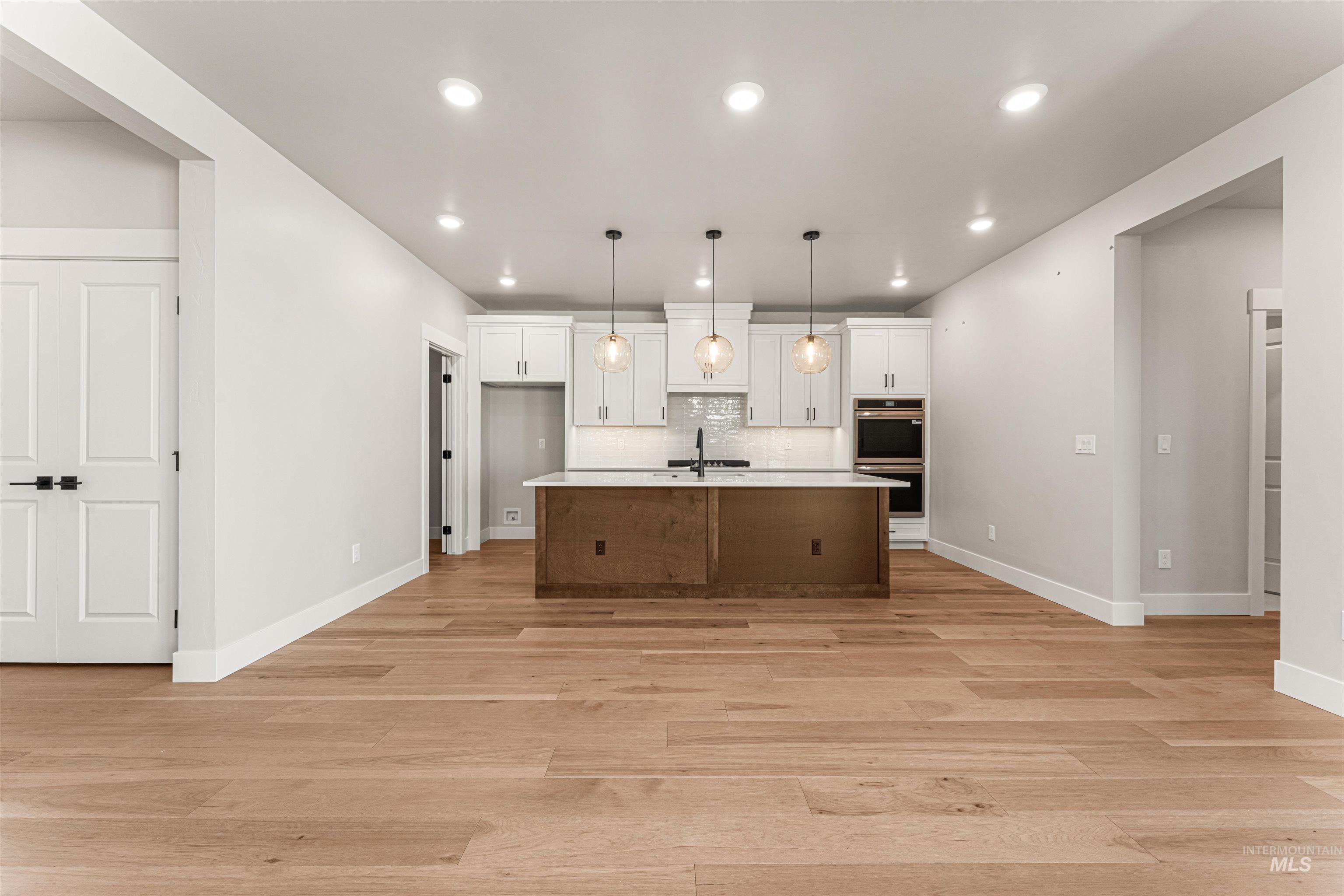 Kitchen featuring light wood-style flooring, white cabinets, recessed lighting, light countertops, and double oven