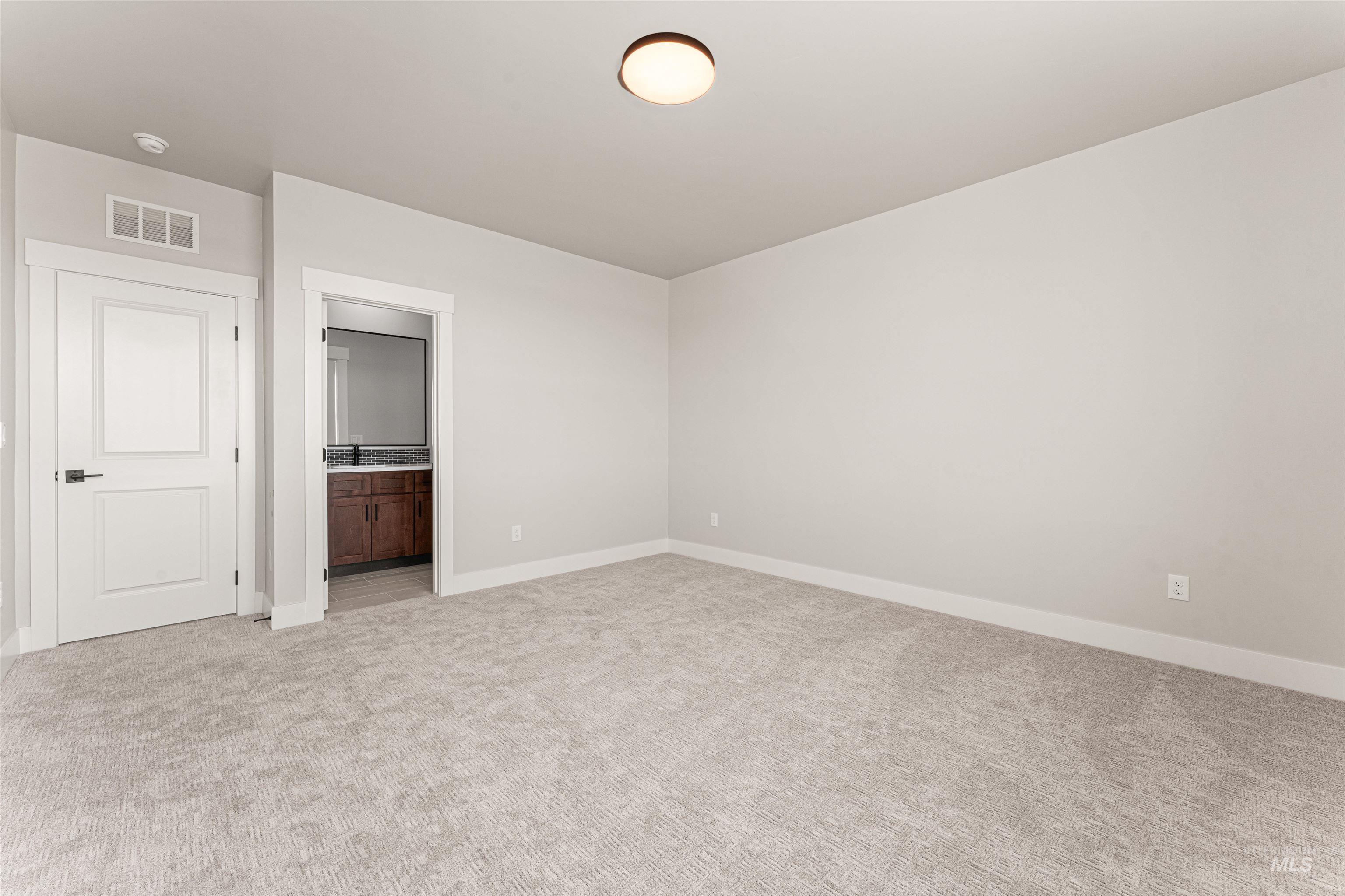 Unfurnished bedroom with light colored carpet and connected bathroom