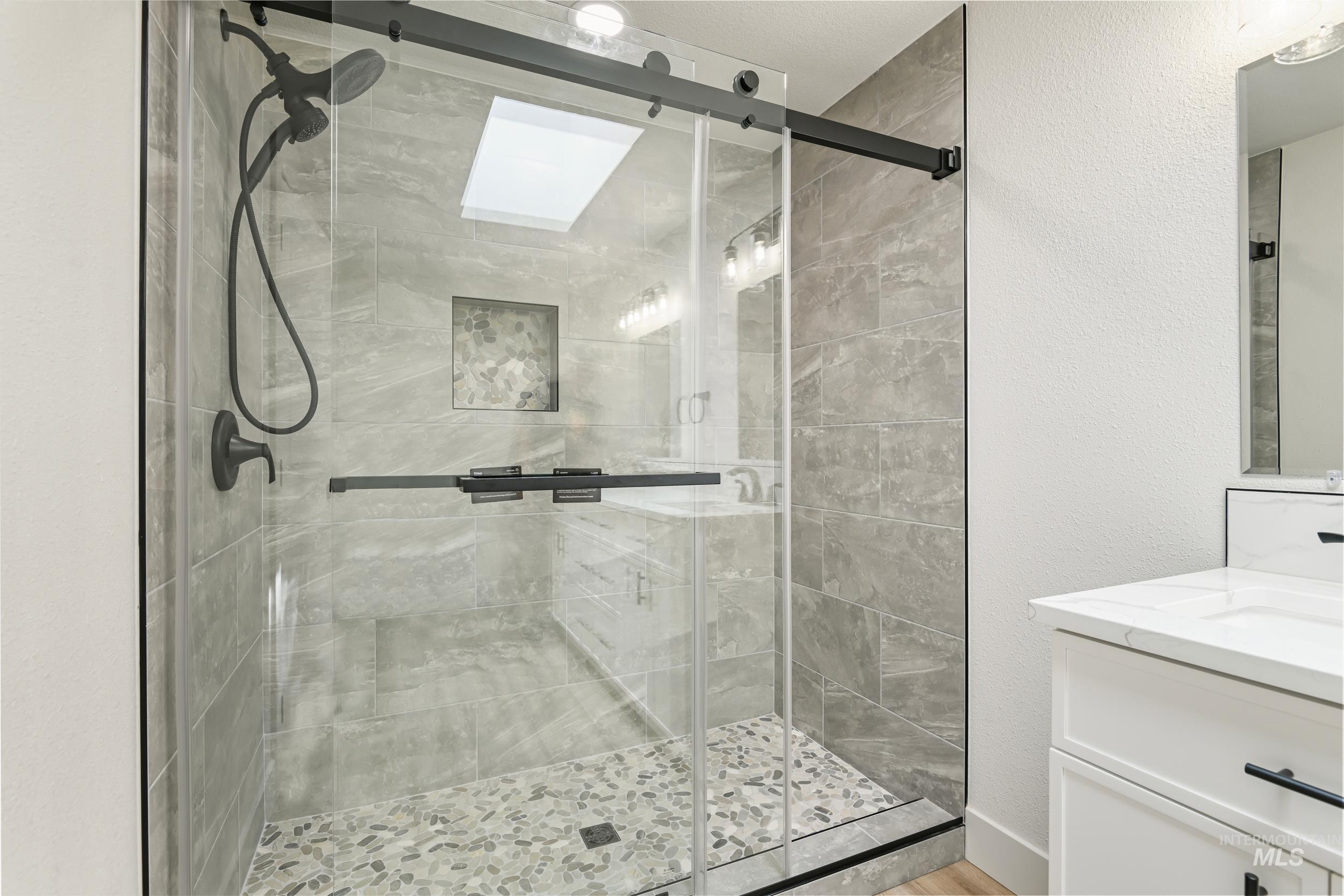 Bathroom with a textured wall, vanity, and a shower stall
