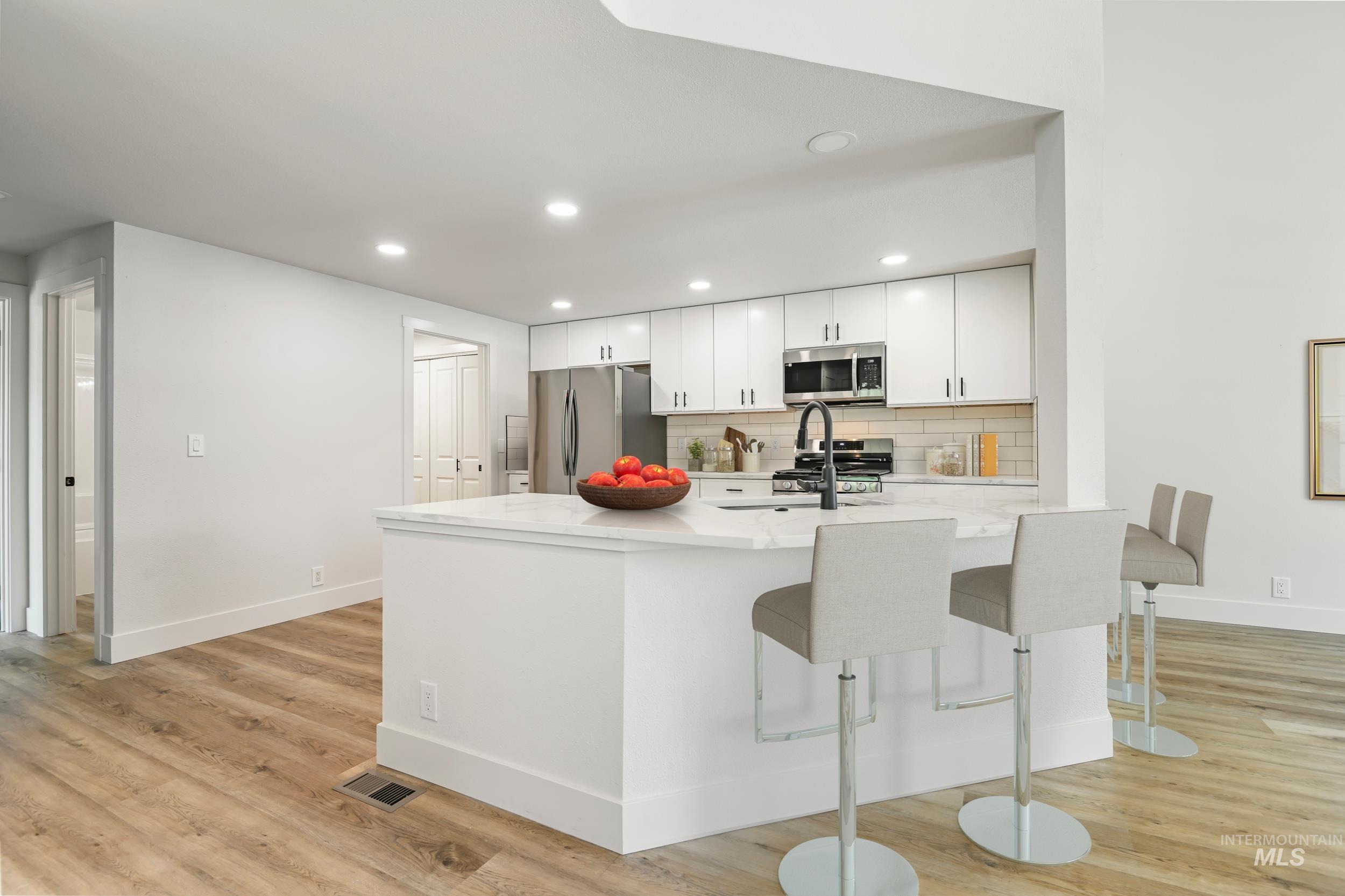 Kitchen featuring tasteful backsplash, recessed lighting, light stone countertops, white cabinetry, and stainless steel appliances