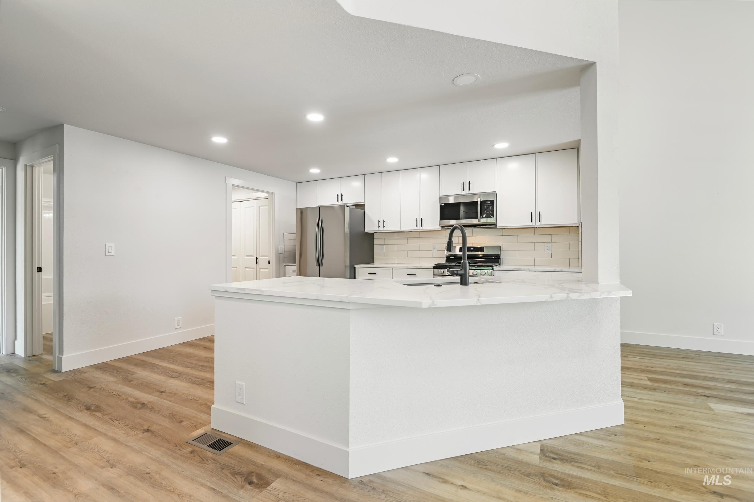 Kitchen featuring tasteful backsplash, recessed lighting, light stone countertops, white cabinets, and stainless steel appliances