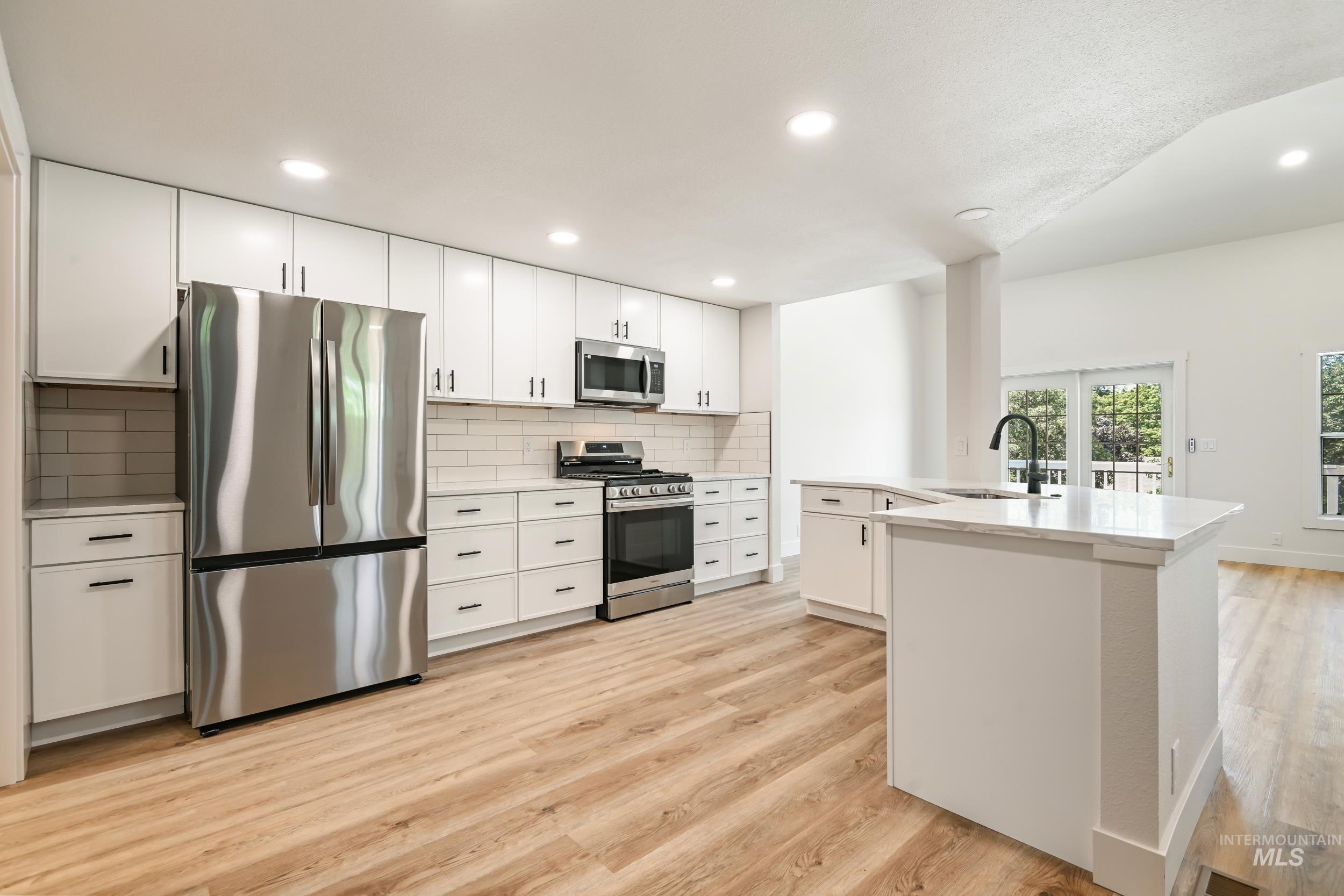 Kitchen with appliances with stainless steel finishes, recessed lighting, tasteful backsplash, white cabinetry, and light wood-type flooring