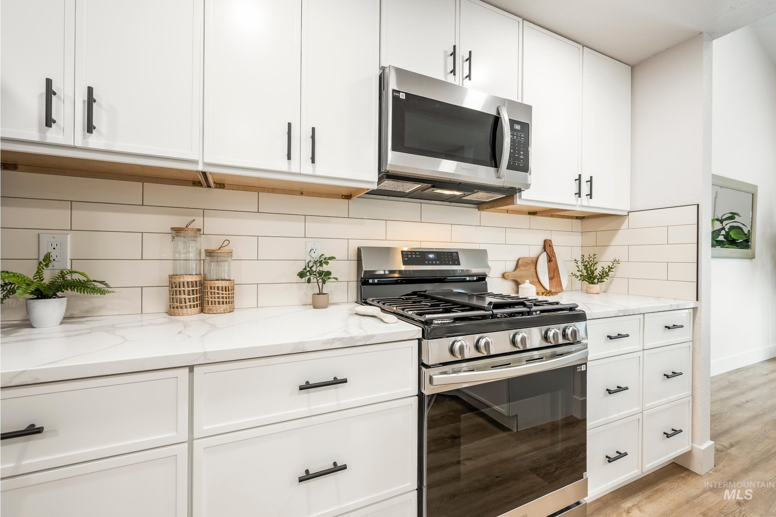 Kitchen with appliances with stainless steel finishes, white cabinets, light stone countertops, and tasteful backsplash