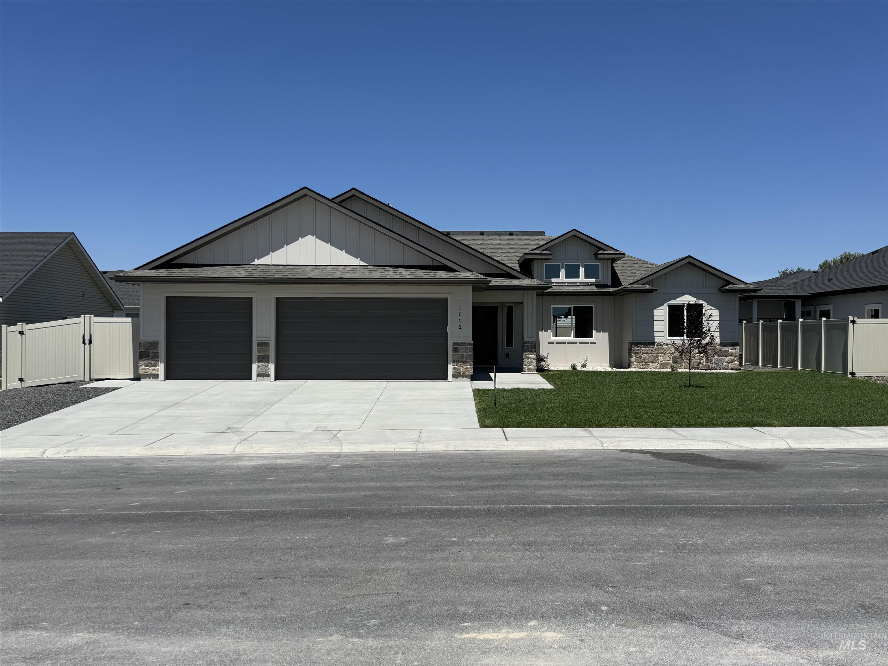 View of front facade with board and batten siding, an attached garage, stone siding, driveway, and a gate