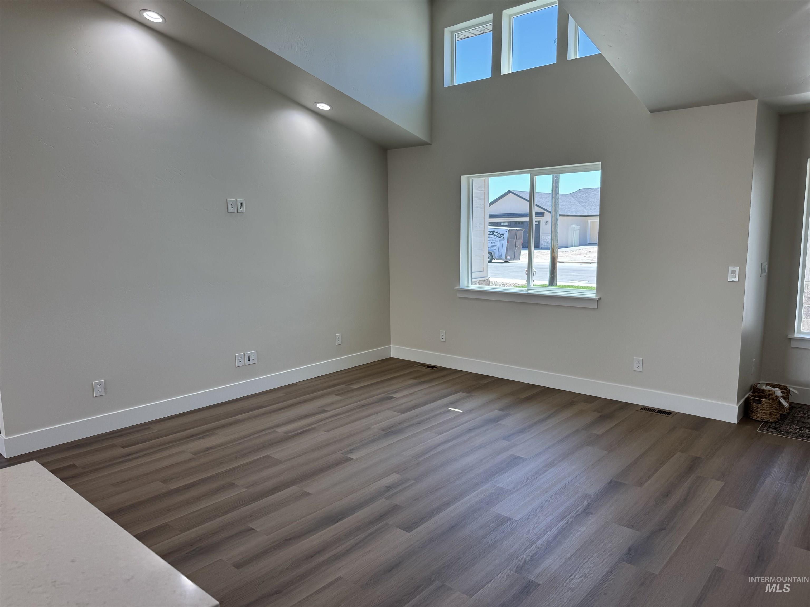 Empty room featuring dark wood finished floors, a towering ceiling, and recessed lighting