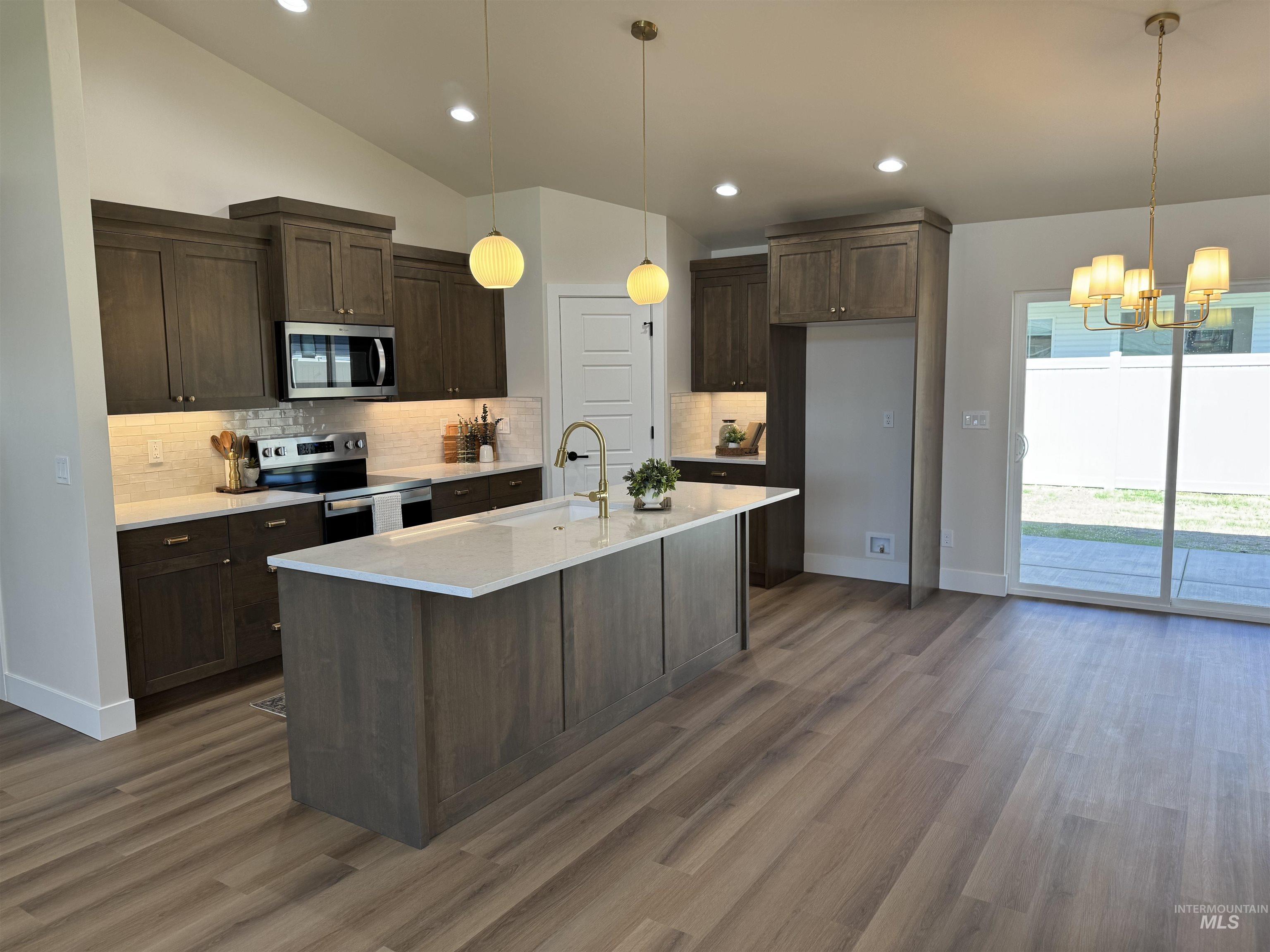 Kitchen with stainless steel appliances, a chandelier, tasteful backsplash, dark brown cabinetry, and wood finished floors
