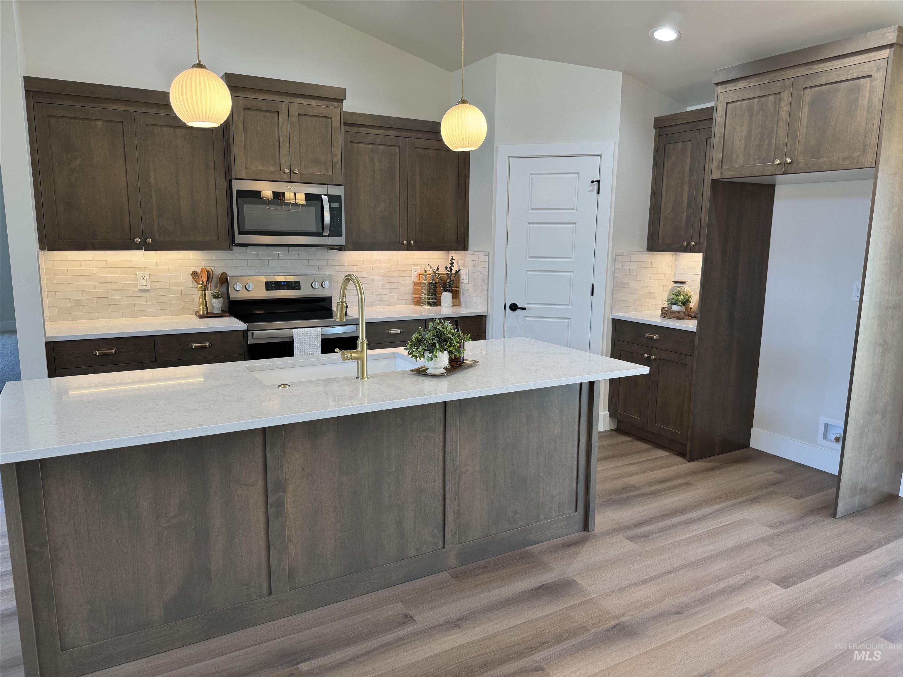 Kitchen with appliances with stainless steel finishes, lofted ceiling, light wood-style flooring, dark brown cabinetry, and decorative backsplash