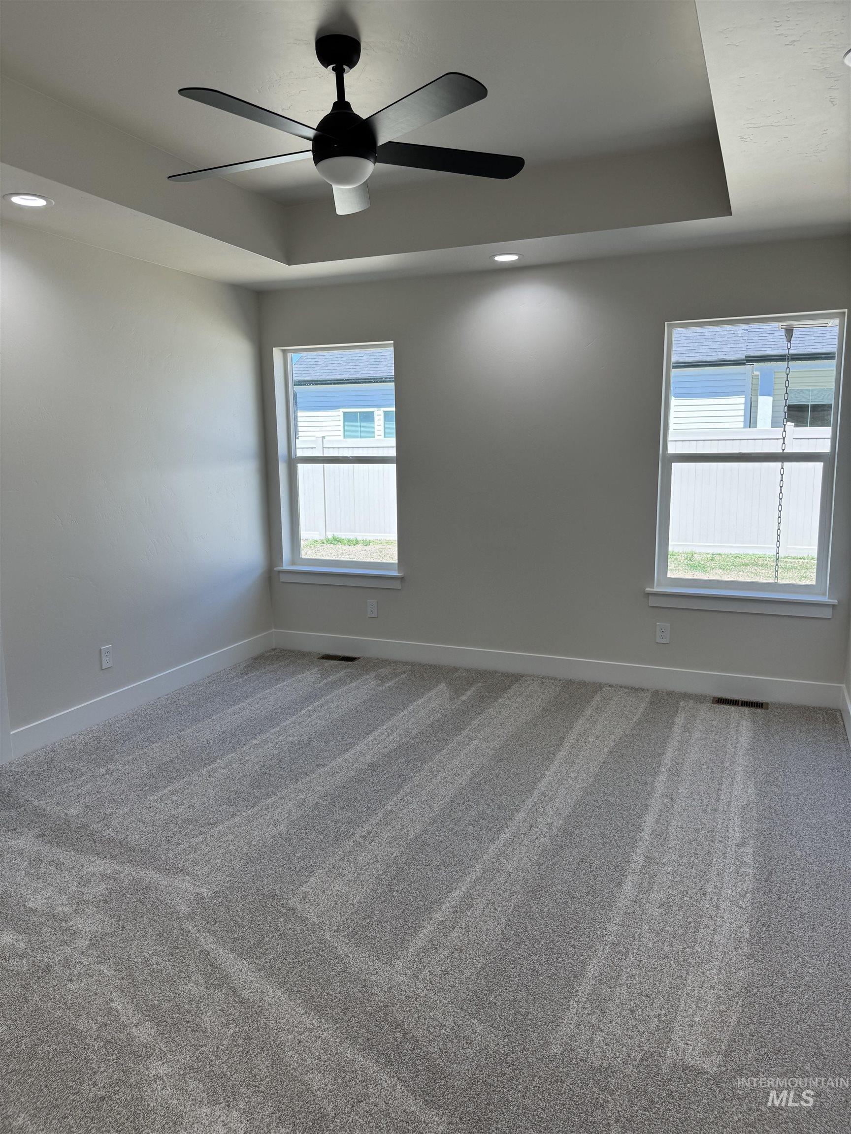 Carpeted spare room with a raised ceiling, ceiling fan, and recessed lighting