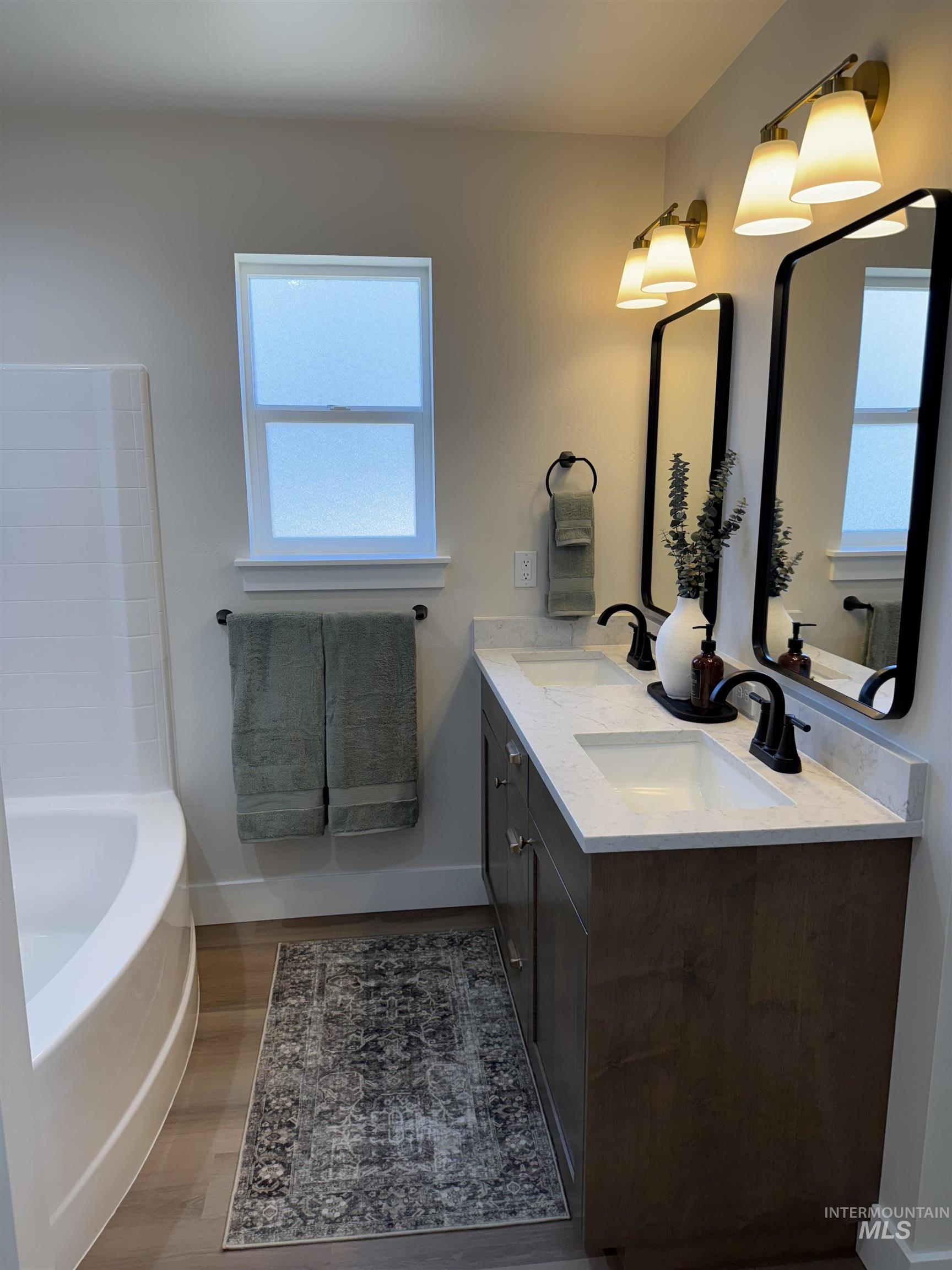 Full bathroom featuring wood finished floors, double vanity, and a tub
