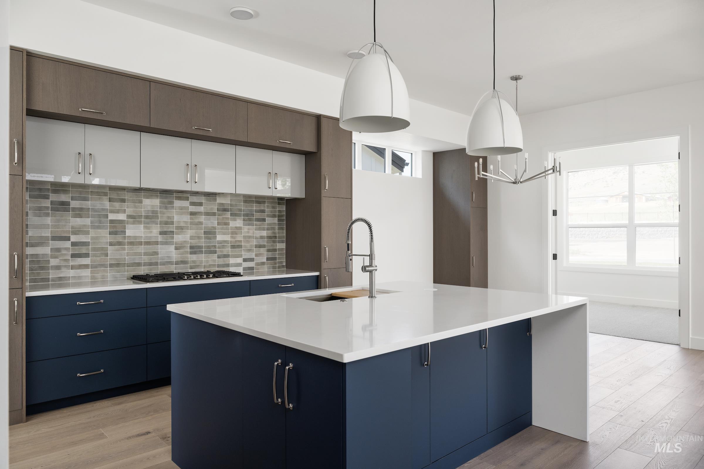 Kitchen with light countertops, backsplash, light wood-type flooring, blue cabinetry, and a center island with sink