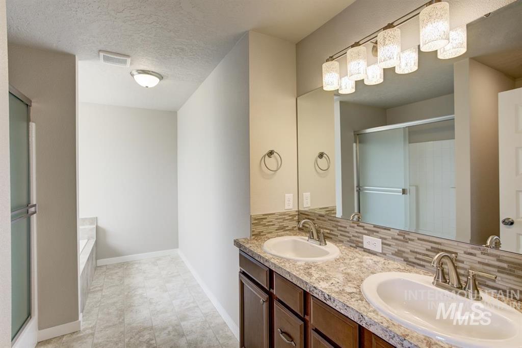 Bathroom with a shower stall, double vanity, a bath, backsplash, and a textured ceiling