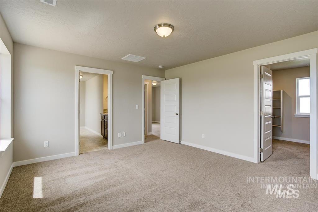 Unfurnished bedroom featuring carpet, a walk in closet, connected bathroom, and a textured ceiling