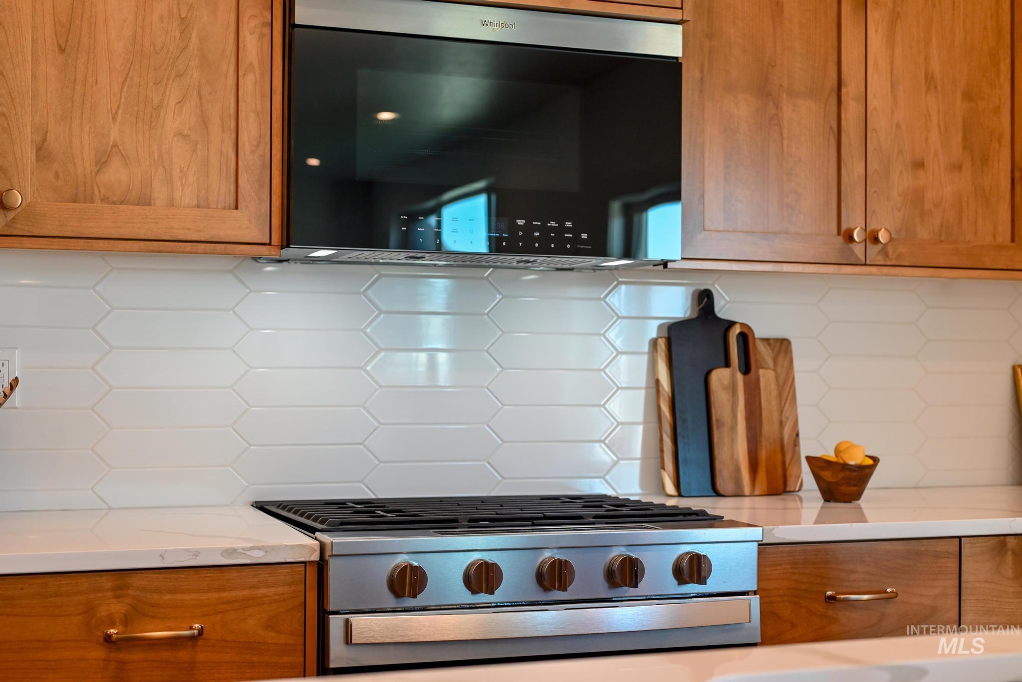 Kitchen featuring stainless steel appliances, tasteful backsplash, brown cabinetry, and light stone countertops