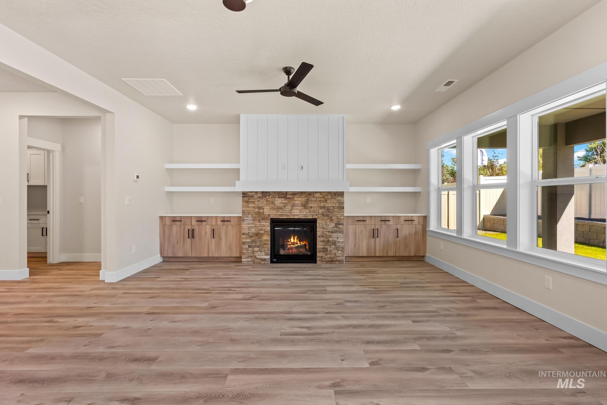 Unfurnished living room featuring a stone fireplace, light wood-style floors, built in shelves, a ceiling fan, and recessed lighting