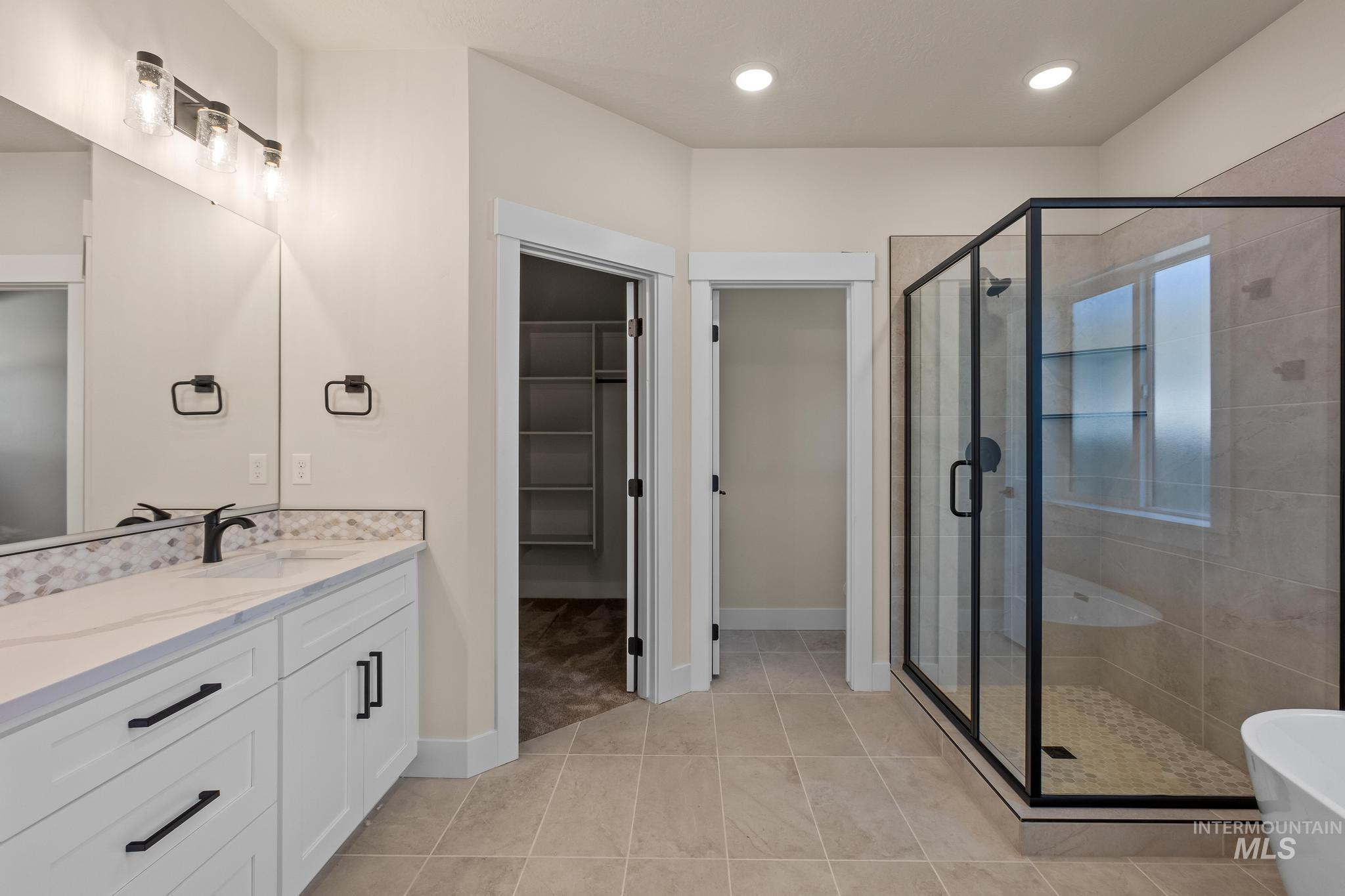 Bathroom featuring a walk in closet, Tiled shower, dual vanities, a freestanding bath, and recessed lighting